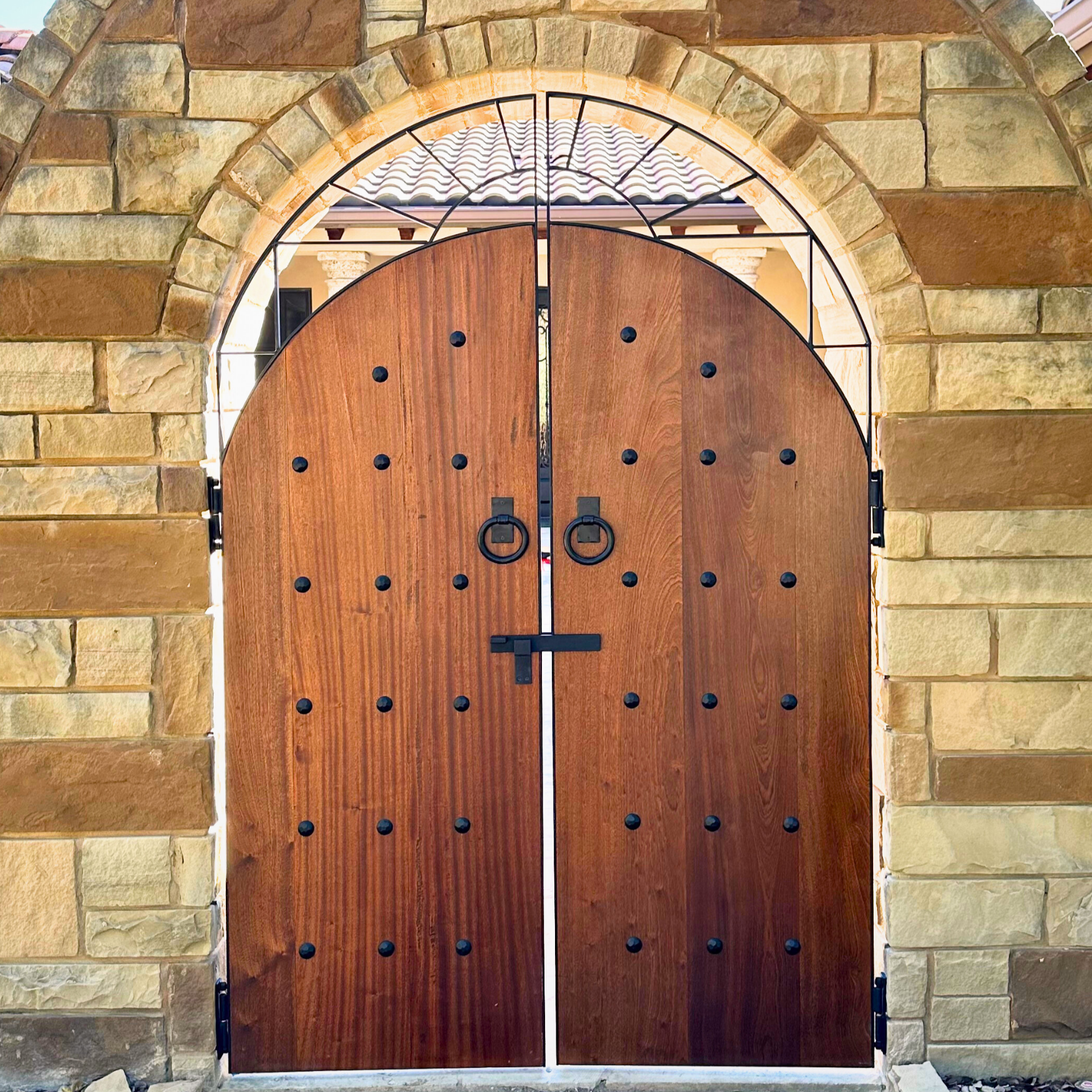 Wooden gate framed in mild steel with circular handles and decorative elements, set within a stone archway.