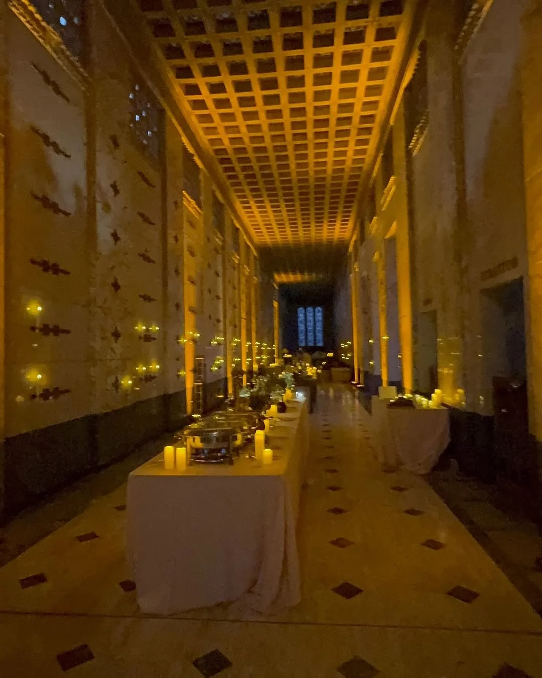 Long hall in a church or cathedral decorated for a memorial or funeral with candles, flowers, and table with chafing dishes.