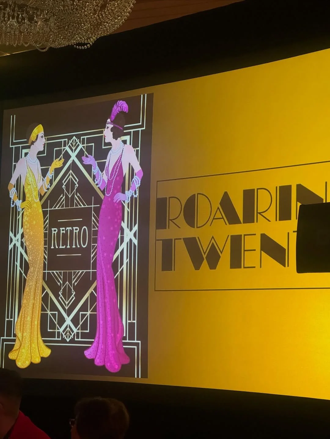 An animated digital illustration of two women dressed in 1920s flapper-style clothing, with pearls, gloves, and headpieces, engaging in conversation against a geometric art deco background. The words 'Retro' and 'Roaring Twenties' are visible, indica
