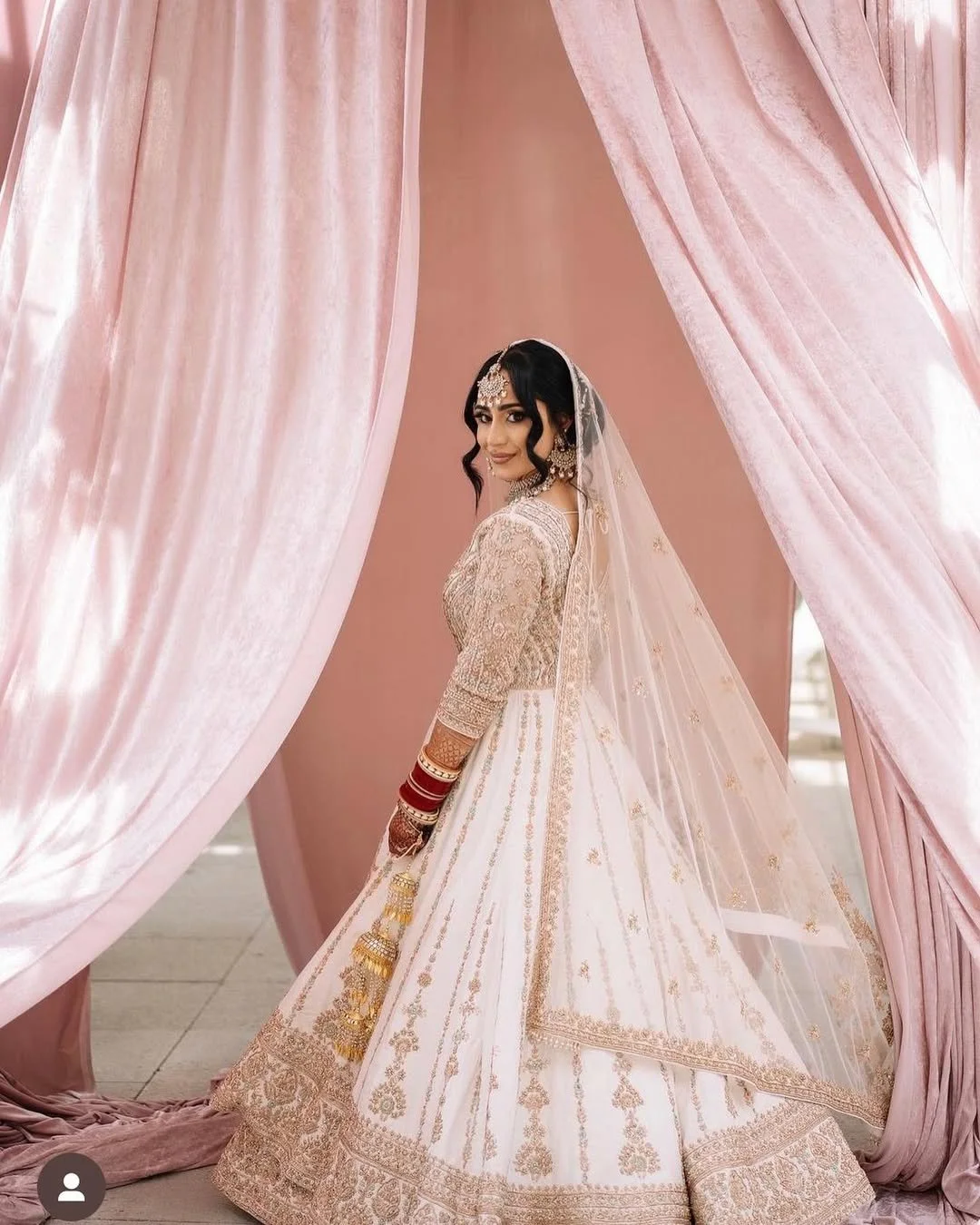 A bride in a traditional wedding dress standing next to pink curtains.