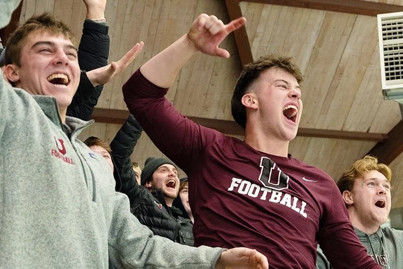 Group of young people cheering enthusiastically at an indoor event, some raising their hands and shouting.
