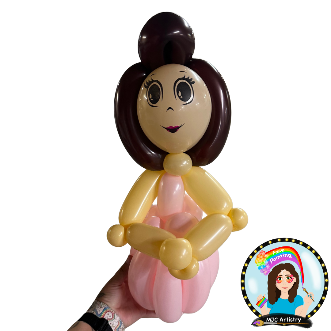 Balloon sculpture of a girl with brown hair, big eyes, and a pink dress, sitting with her hands on her lap.