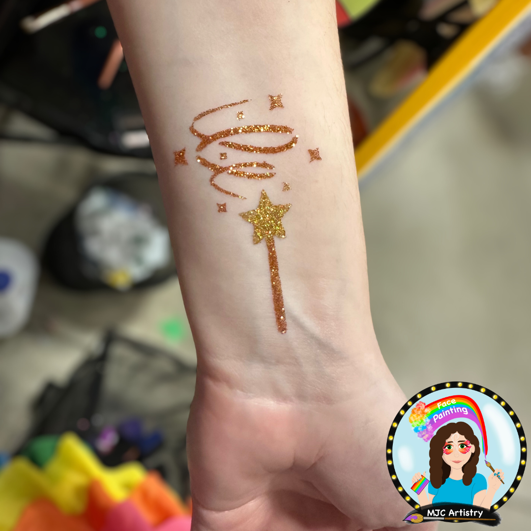 A glittery temporary tattoo of a magic wand with a star at the tip, surrounded by swirling lines and small stars, on a person's forearm. Glitter tattoos at an event in Vancouver.