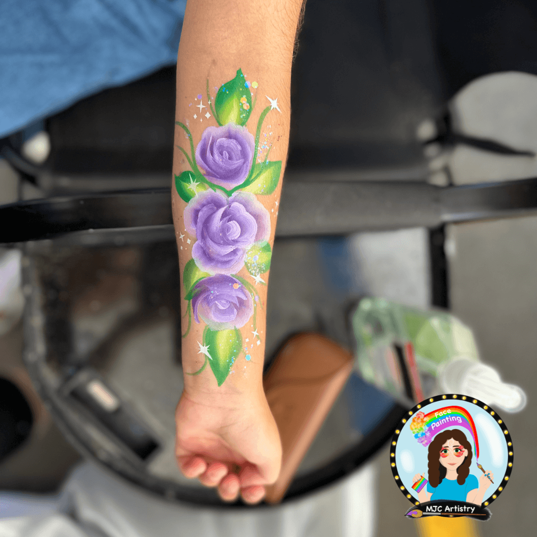 Arm with a vibrant purple flower and green leaves painted as a tattoo design.