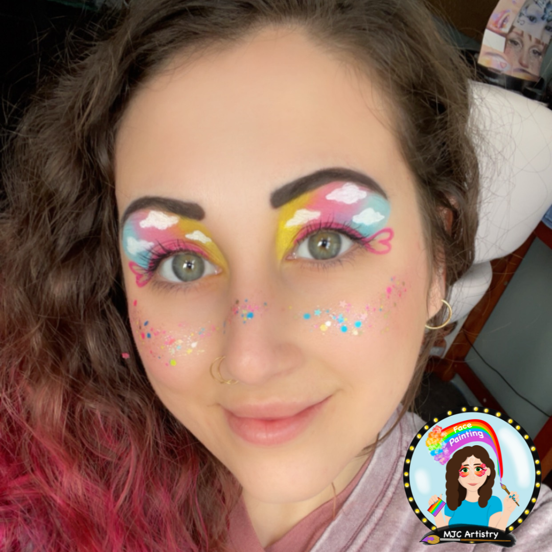 Woman with colorful, cloud-themed eye makeup and rainbow-themed face paint, including glitter and small stars on cheeks.