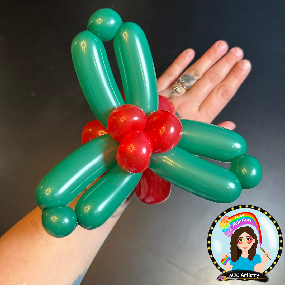 A person wearing a balloon sculpture resembling a dragonfly on their hand, with a black background.