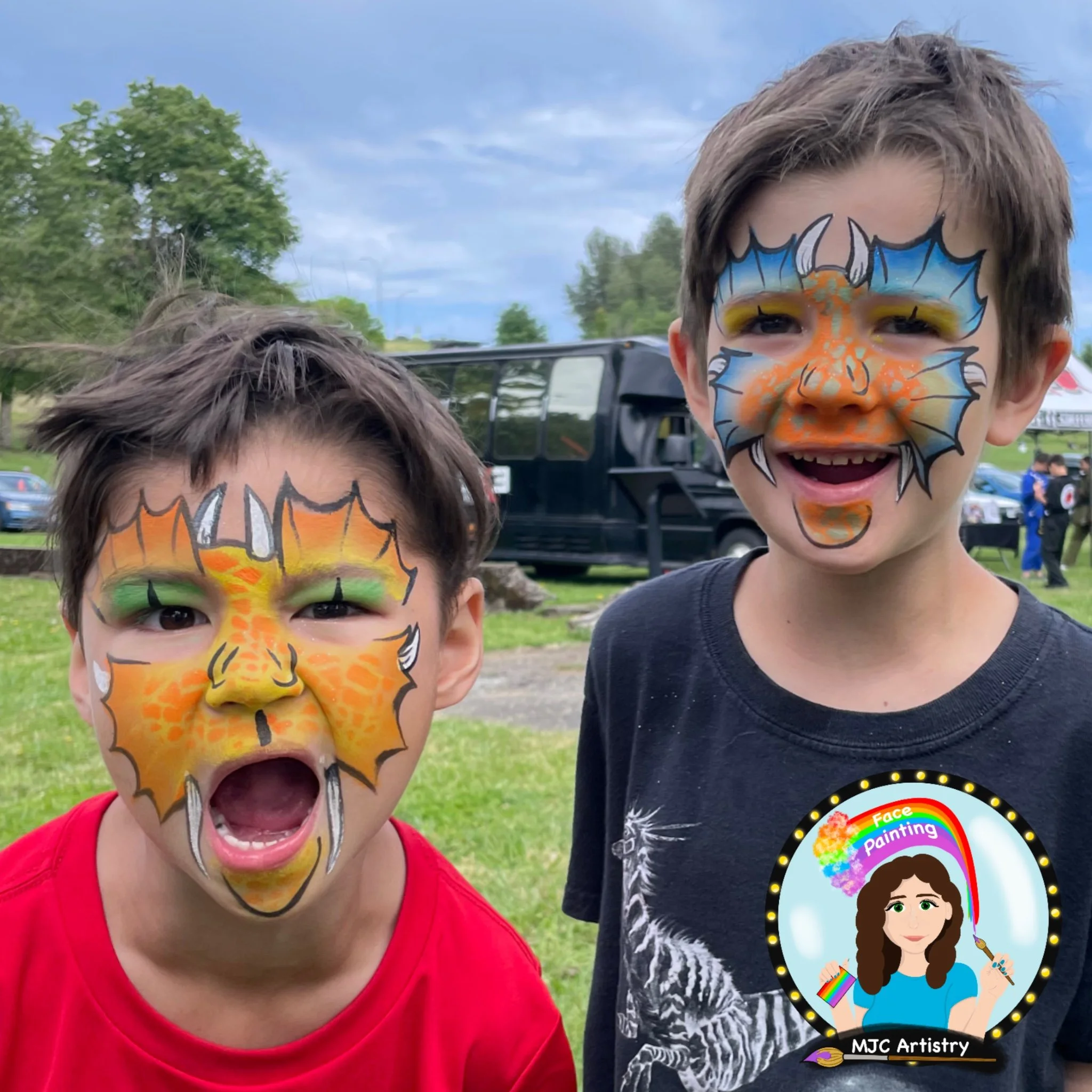 Two young boys with colorful dragon-themed face paint, one wearing a red shirt with mouth open, the other smiling, outdoors with trees and a black vehicle in the background.