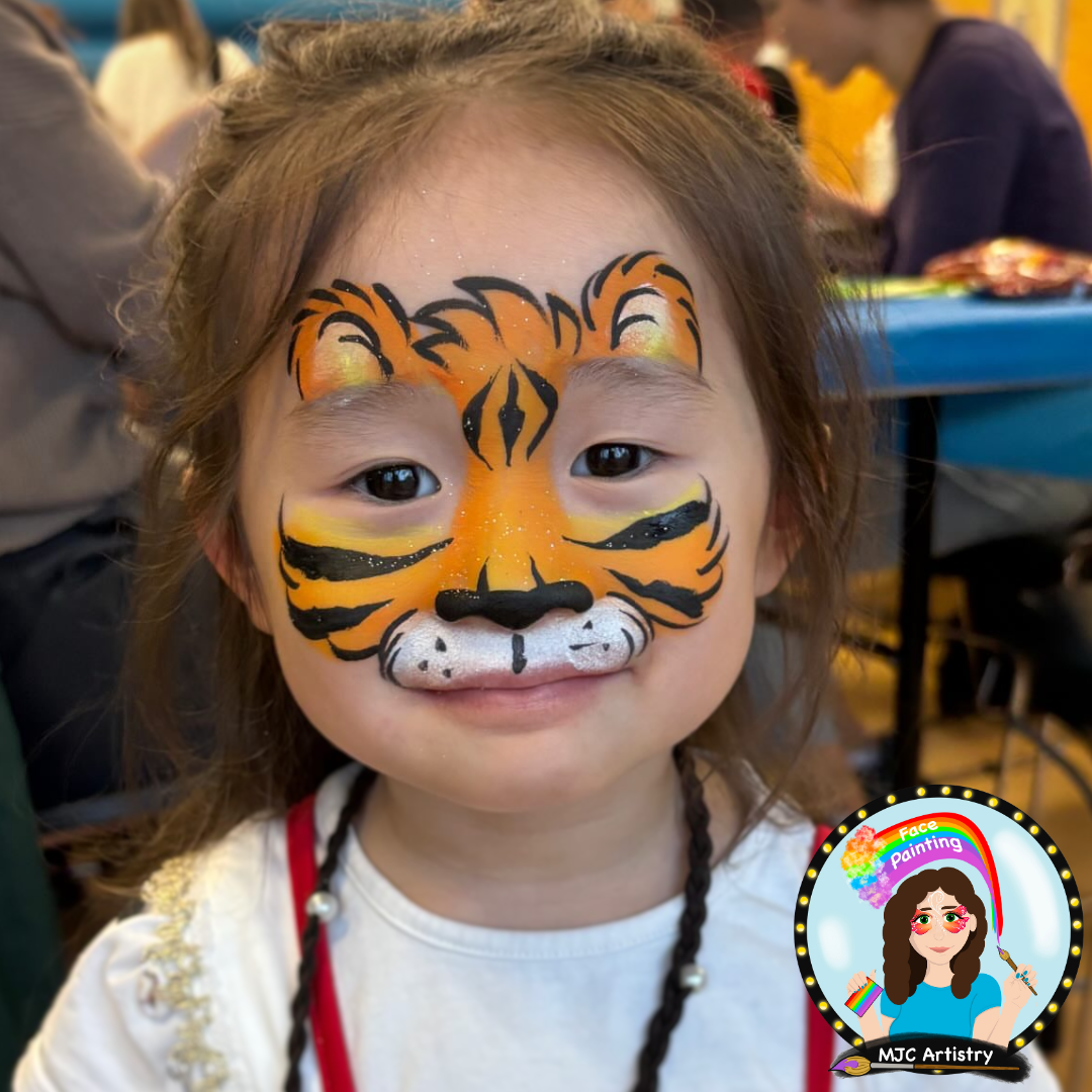 Young girl with face paint resembling a tiger, smiling, with people and tables in the background, face painting at a birthday party in Vancouver. 