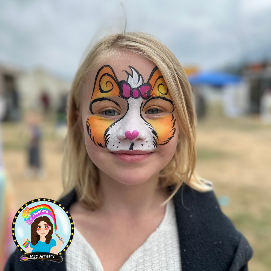 A young girl with face paint of a cute cartoon tiger with orange and white fur, pink nose, purple bow, and yellow accents taken at a festival in Vancouver BC.