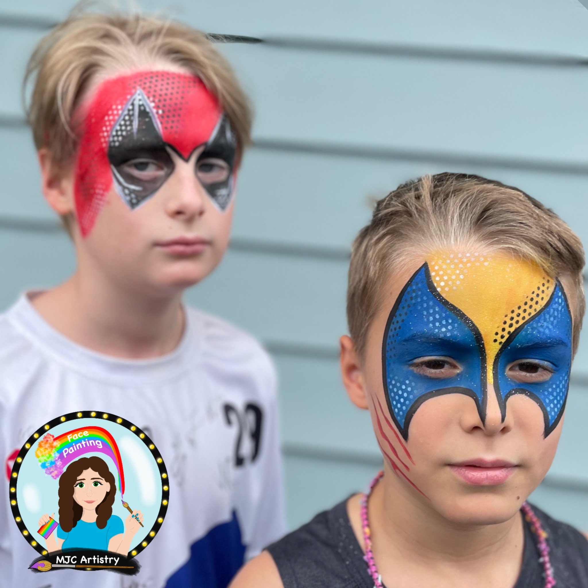 Two children with face paint, one with red and black design, the other with blue and yellow butterfly design. They are standing in front of a light blue horizontal siding background.