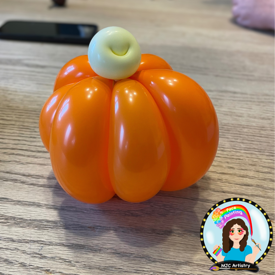 A pumpkin made with orange balloons and a small white balloon on top, arranged on a wooden surface.