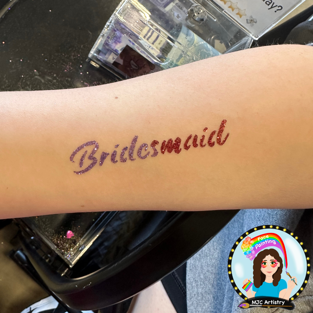 Temporary glitter tattoo on forearm spelling 'Bridesmaid' in purple and red glitter.