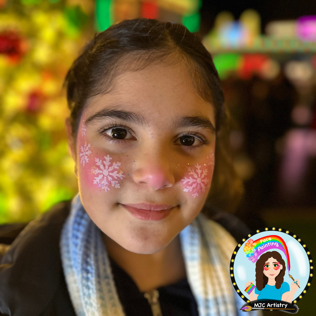 A young girl with face paint of pink snowflakes on her cheeks, smiling at the camera, with colorful background taken at a public event in Vancouver BC.