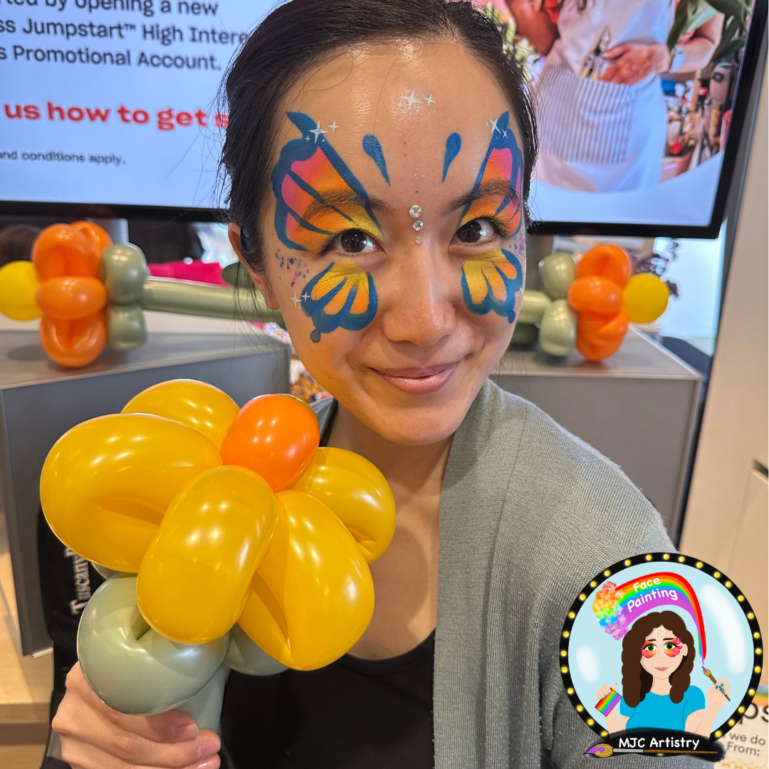 Woman with butterfly face paint holding a balloon flower at face painting event.