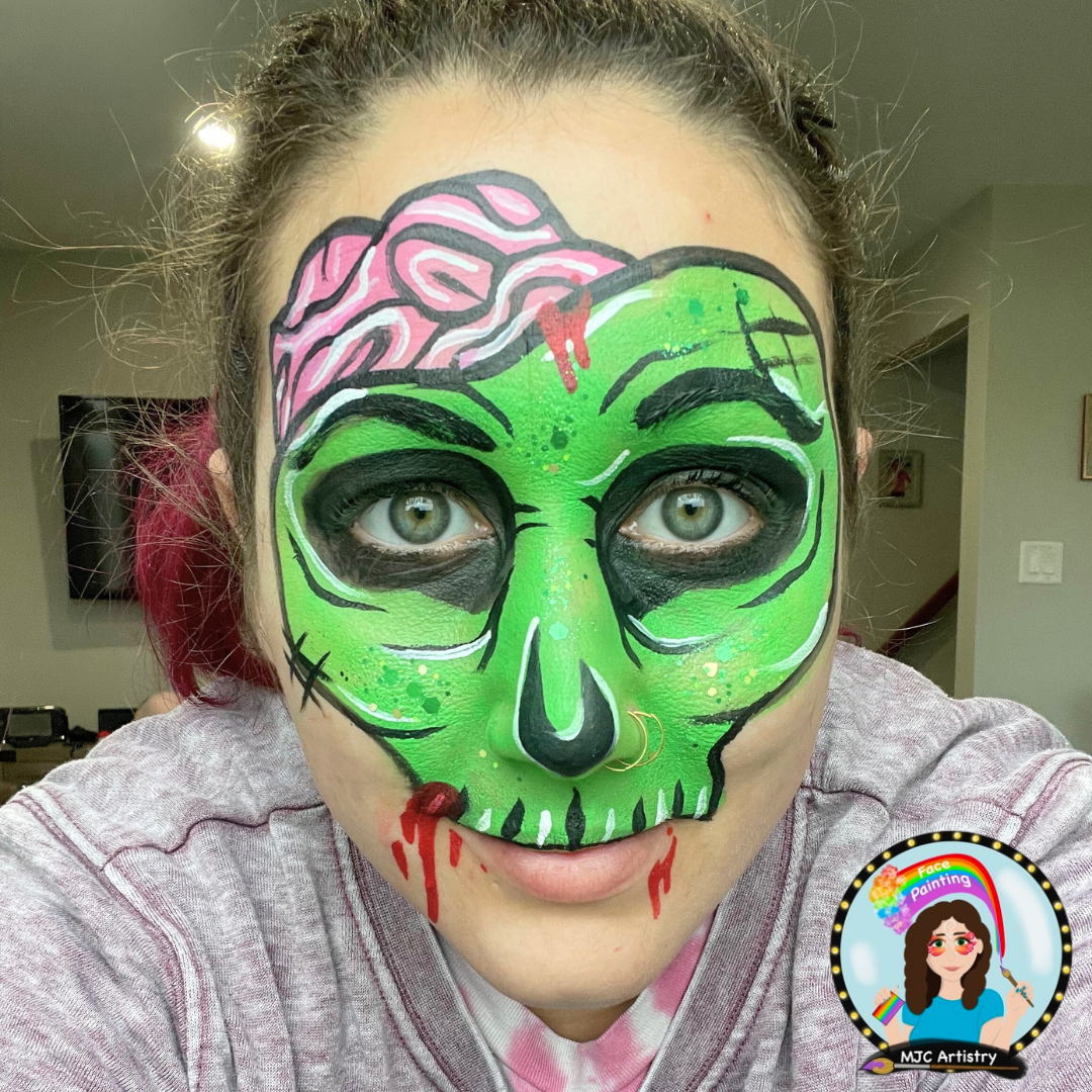 Person with face painted as a green skull with pink brain, black eye sockets, and red dripping effects, wearing a nose ring.