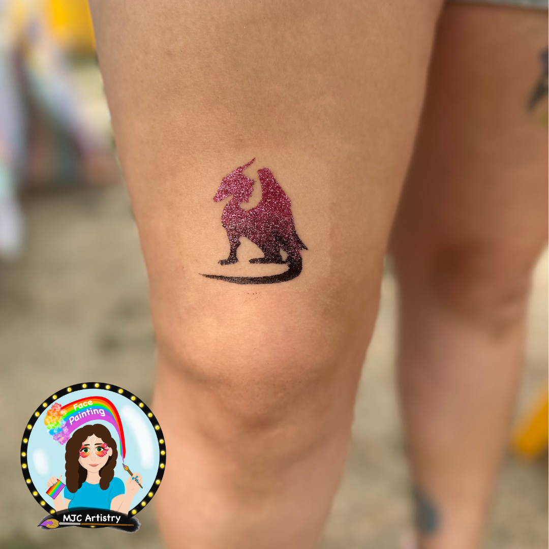 Tattoo of a unicorn in pink and black glitter on a person's thigh.