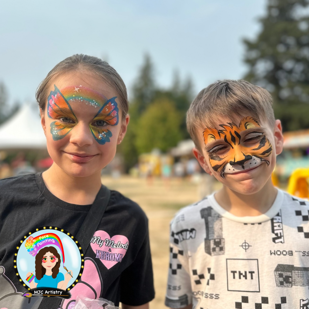 Two children with face paint: a girl with a rainbow and butterfly design and a boy with a tiger face, at an outdoor event on a sunny day in Vancouver BC.