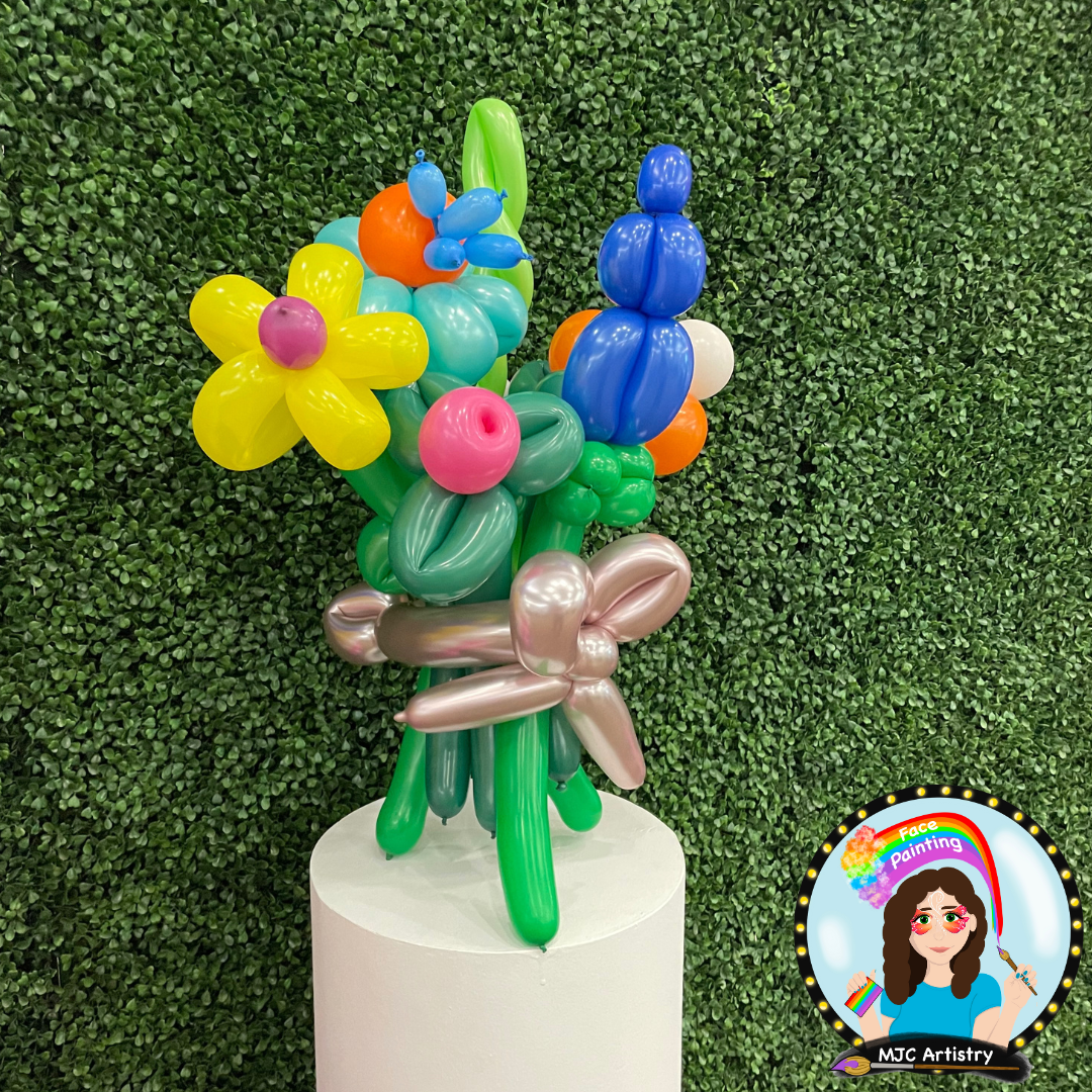 Colorful balloon sculpture of flowers and a butterfly against a green leafy background.