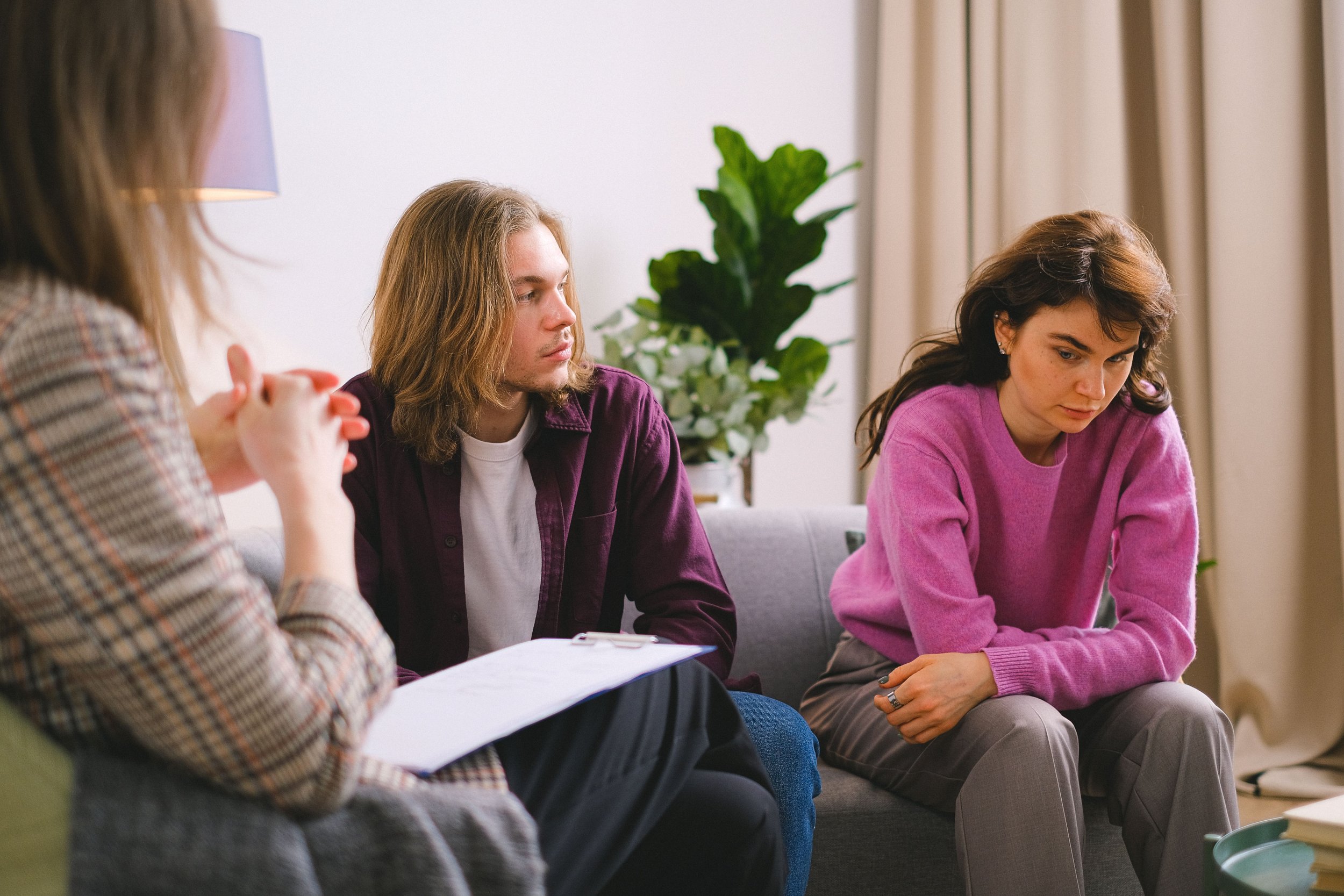 People sitting on a couch, engaged in a discussion, with a woman in a purple sweater leaning forward.