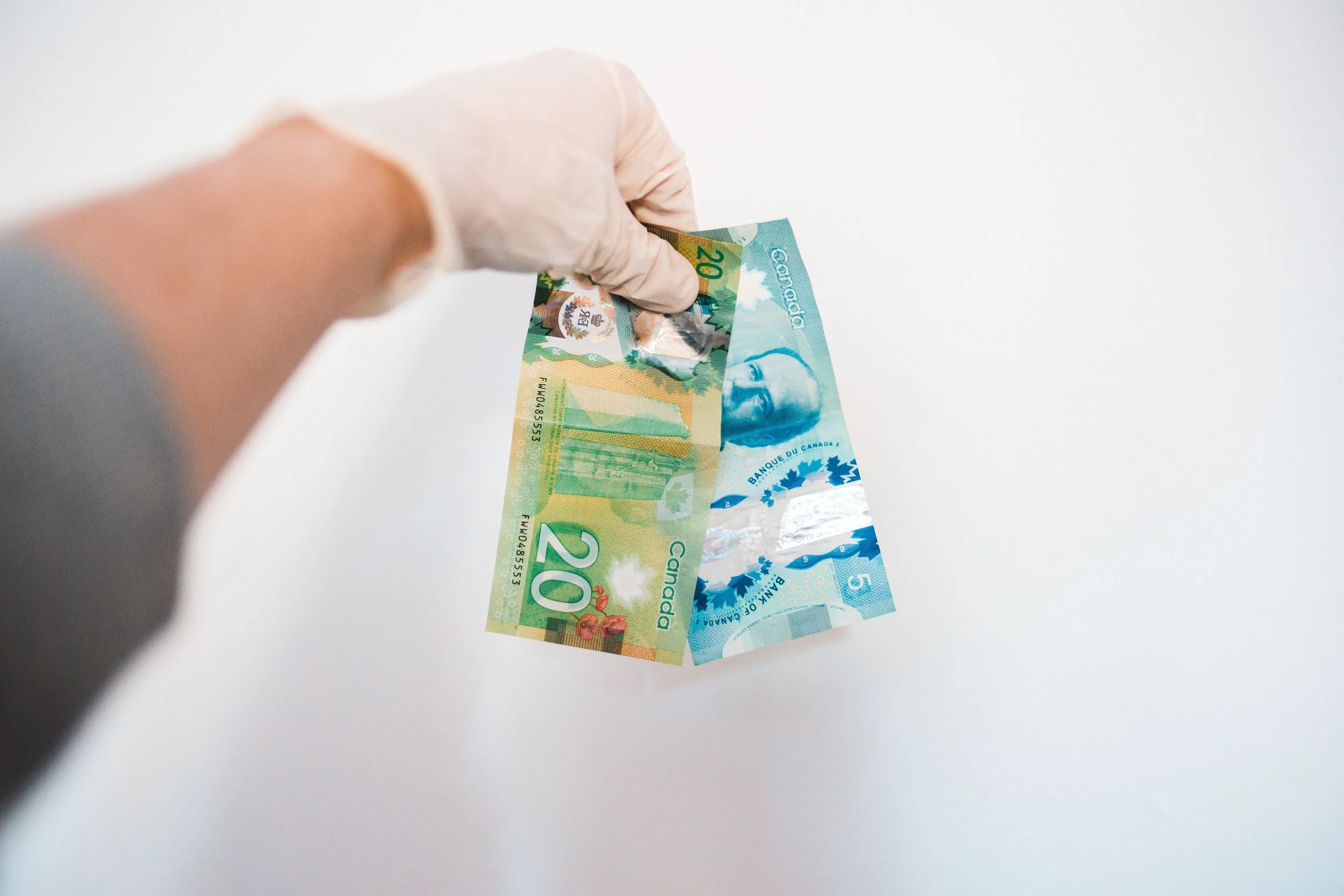 Gloved hand holding Canadian bills against a white background, representing financial safety.