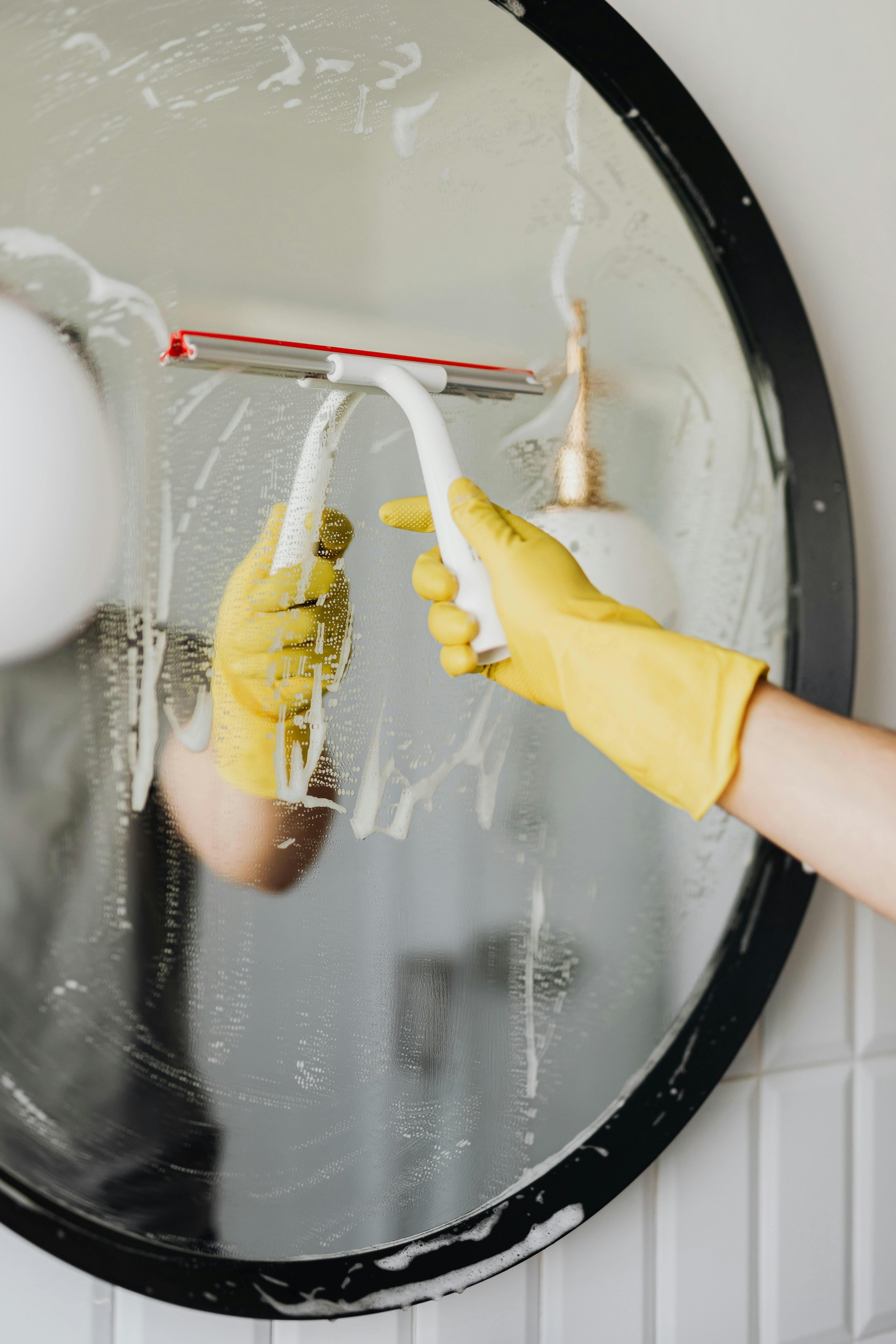 Person wearing yellow rubber gloves cleaning the inside of a washing machine door with a scrubber.