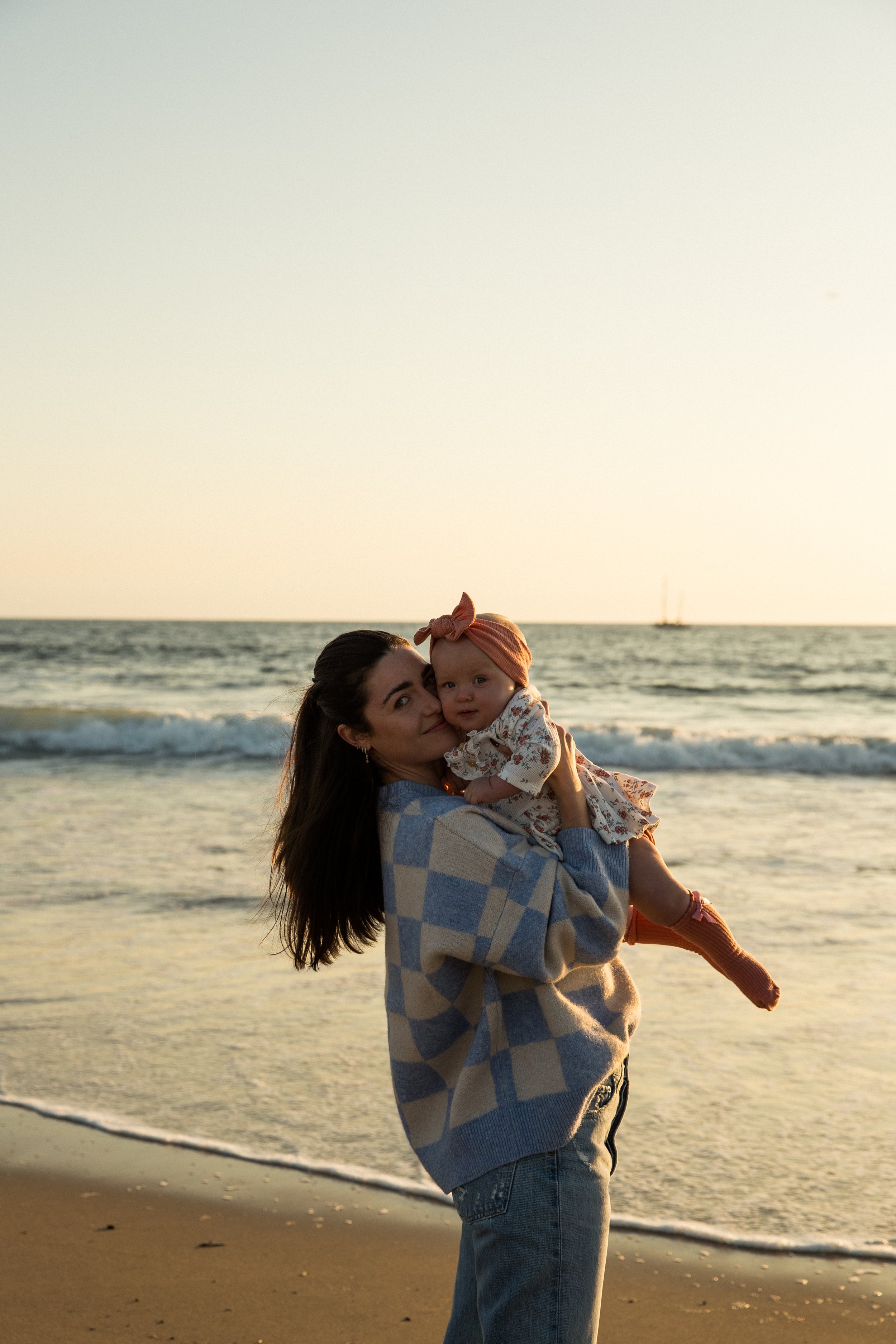 Woman holding a baby on a beach at sunset.