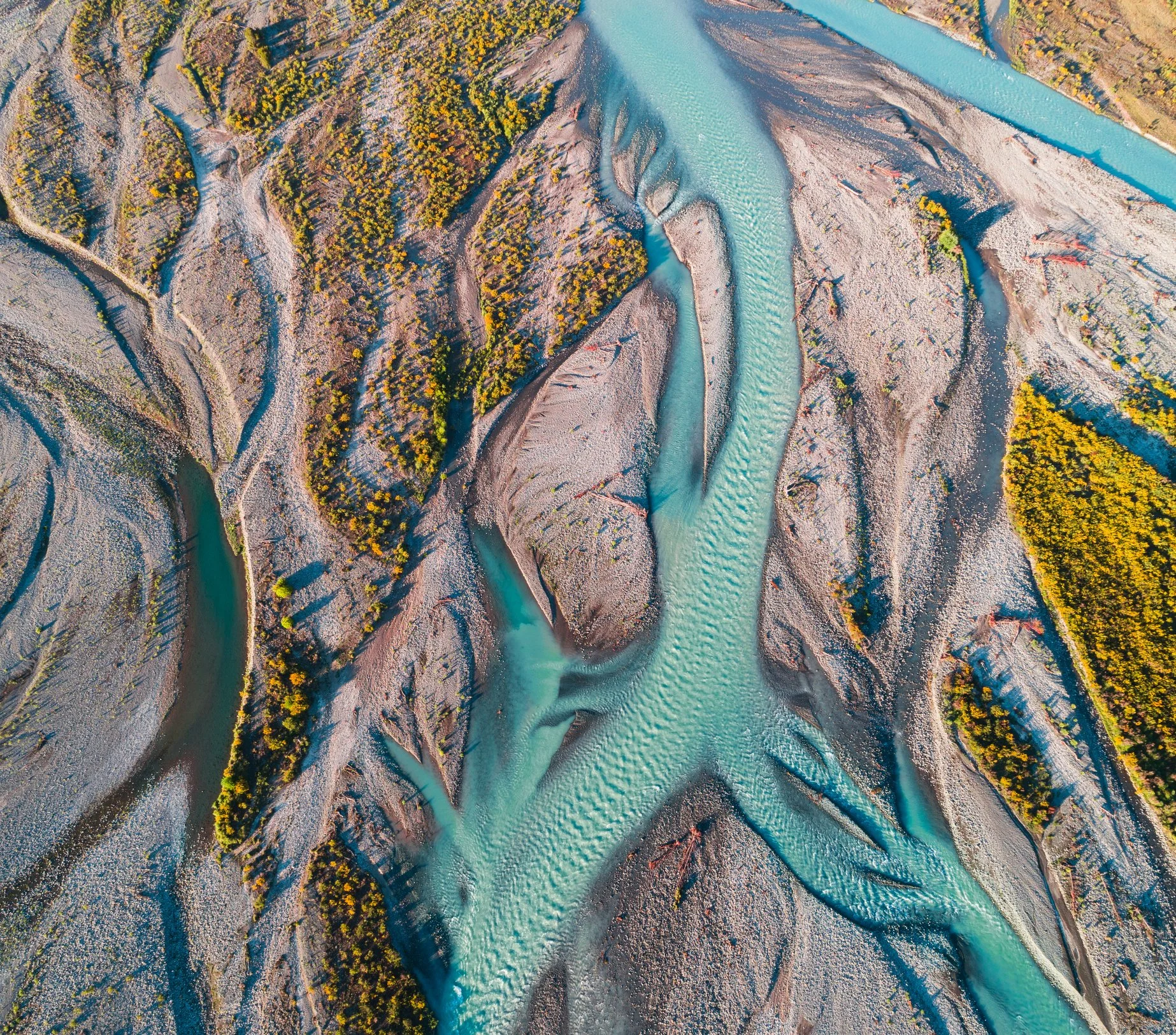 An aerial view of a winding river flowing through a landscape with trees and exposed soil or rocky terrain.