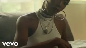 Close-up of a woman wearing multiple layered necklaces, hoop earrings, and a sleeveless top, with a blurred background.