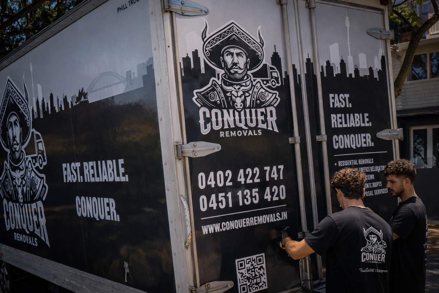 A Conquer Removals truck with company logo and details displayed on the side. Two workers are standing near the truck, with one holding the door handle. The worker's shirt features the same logo as on the truck.