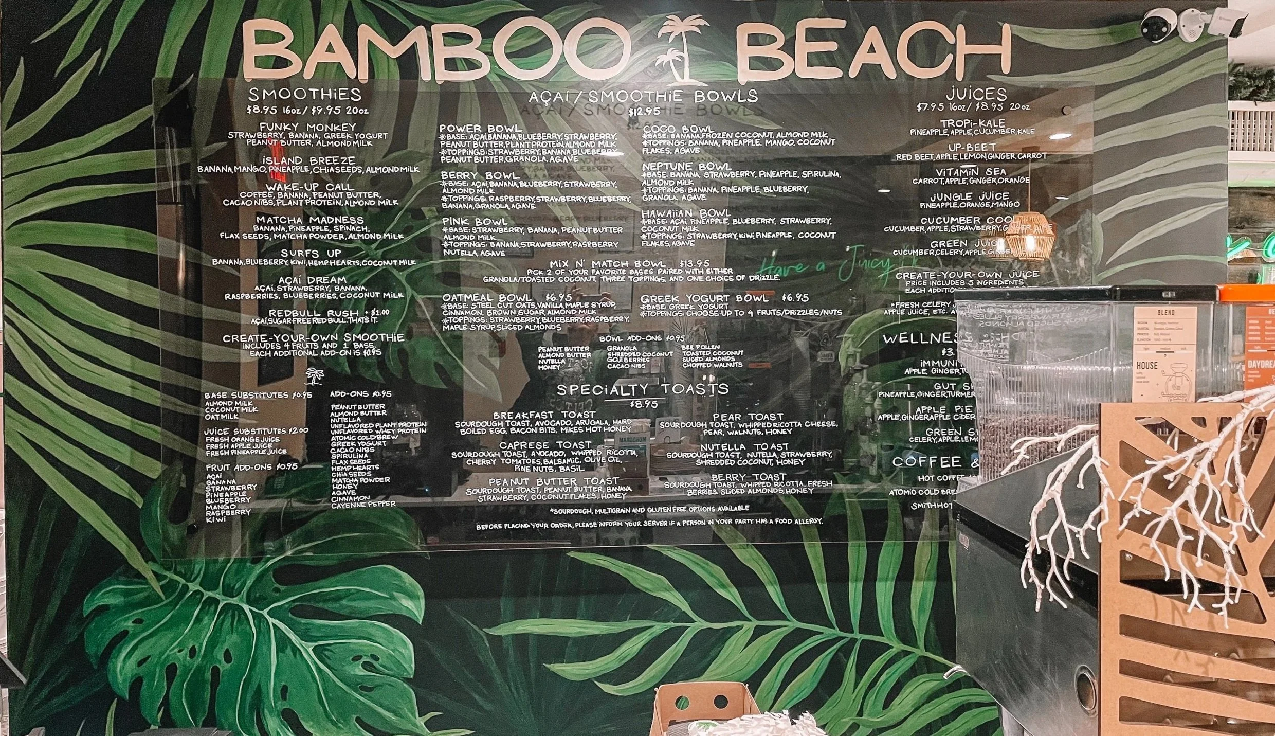 Menu board for Bamboo Beach featuring smoothies, acai bowls, juices, specialty toasts, and coffee, with a tropical green leaf background and palm tree graphics.