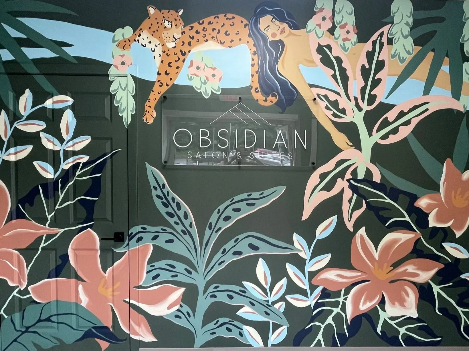 Colorful mural of a woman and a leopard perched among large tropical leaves and flowers, with a sign reading 'Obsidian Salon & Suites' in the center.