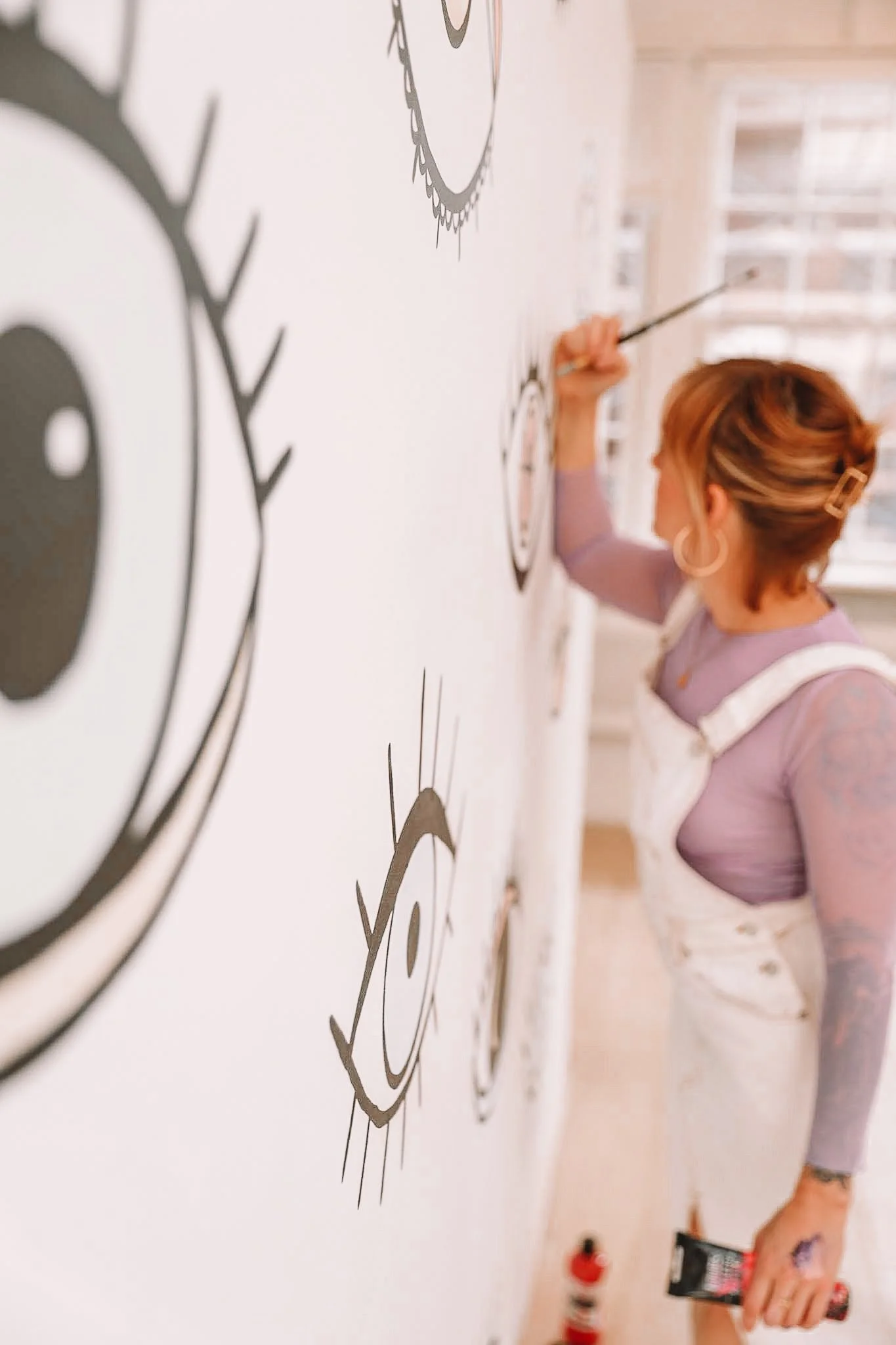 Mural artist Jenna Wells painting a custom black-and-white mural with graphic eye illustrations in a South End Boston studio.
