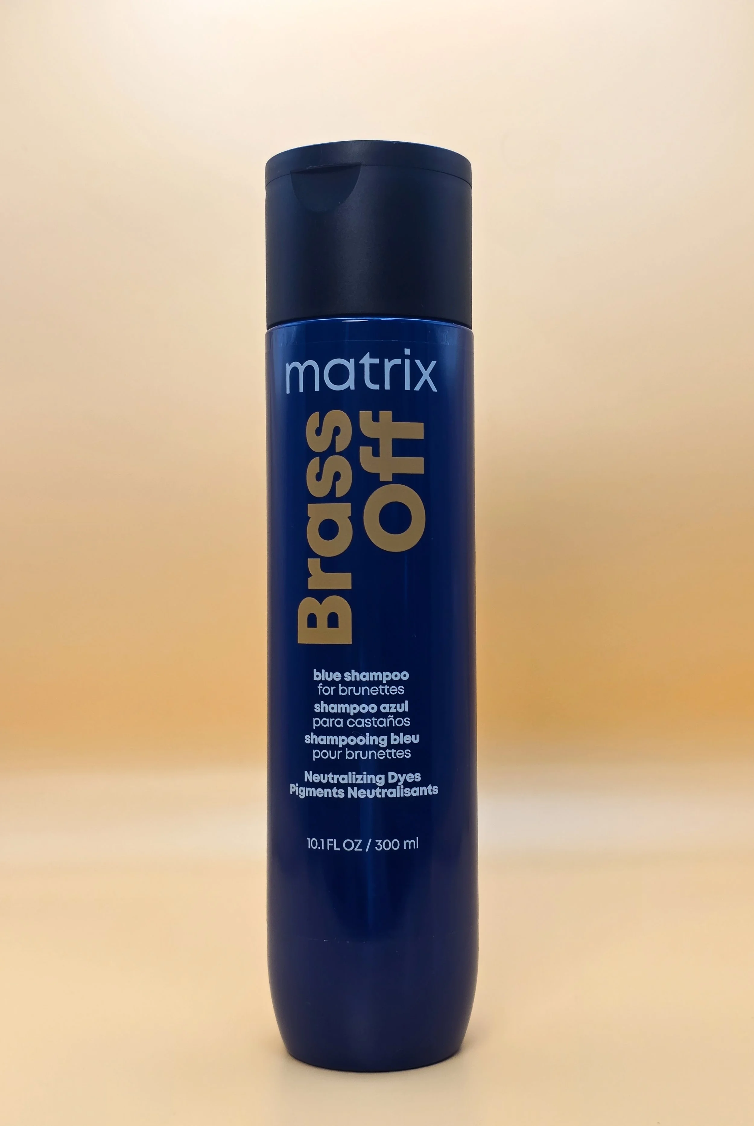 A tall blue can of Matrix Brass Off blue shampoo for brunettes with a dark blue cap, standing upright against a beige background.