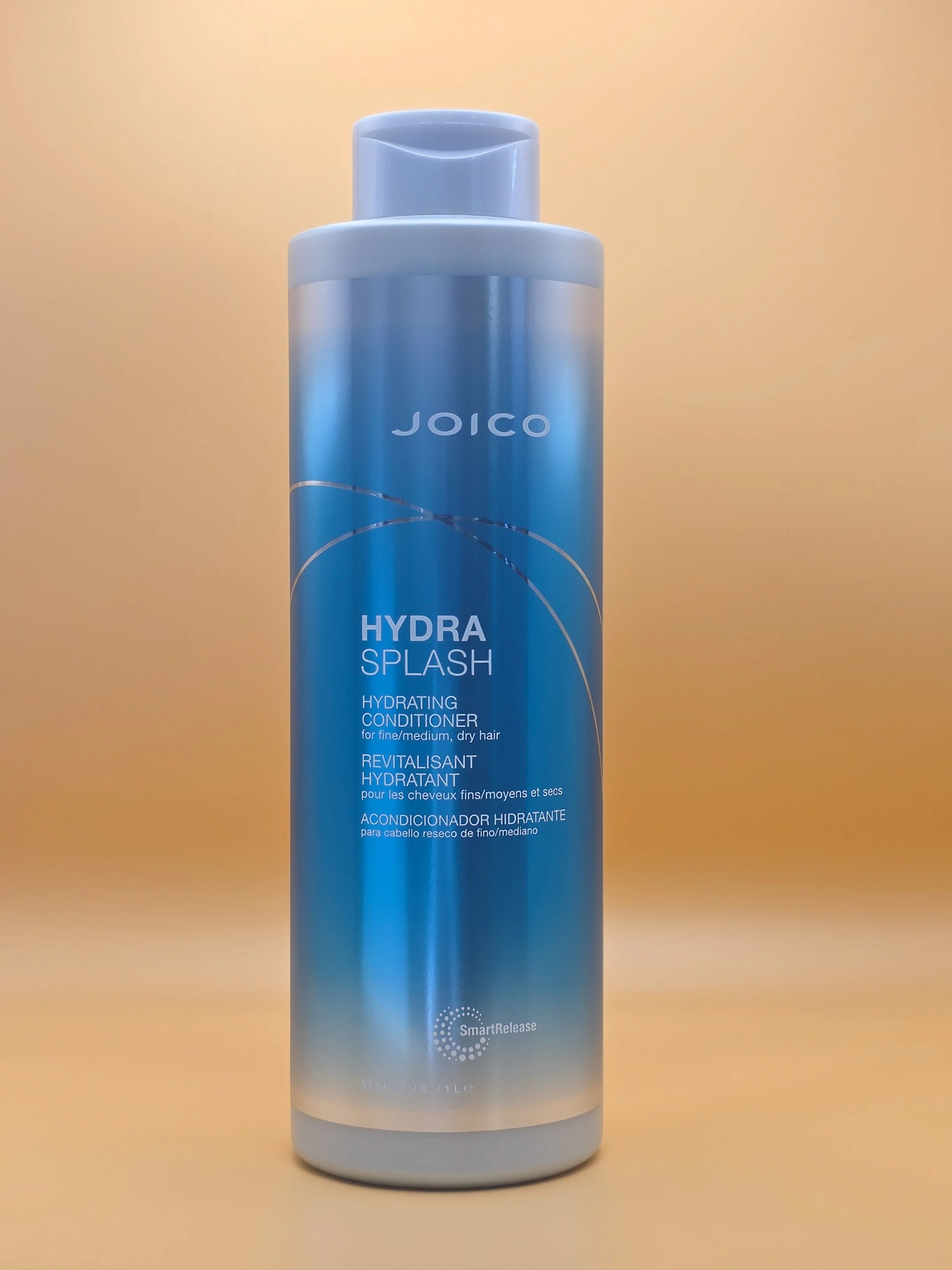 A blue bottle of Joico Hydra Splash hydrating conditioner for fine or medium, dry hair, with a light-colored background.