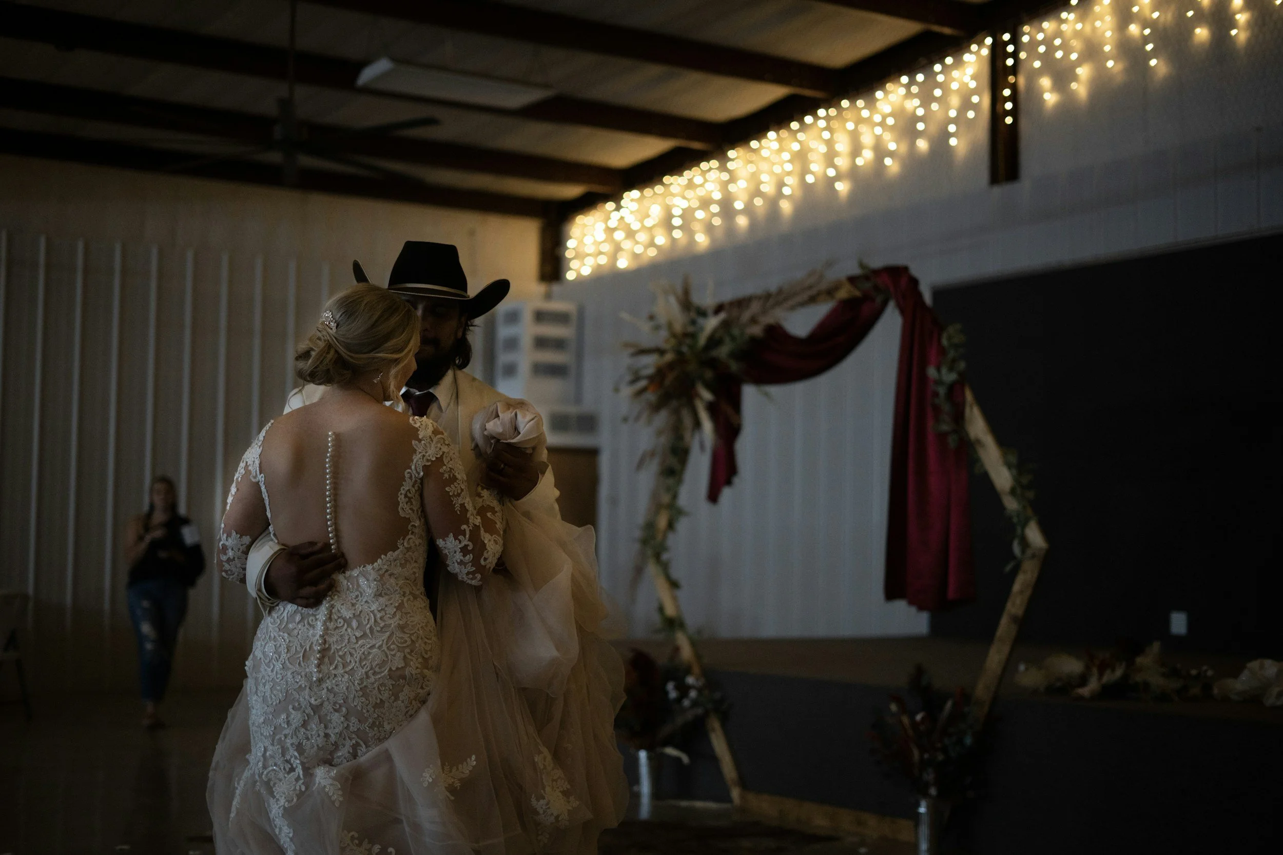 A bride and groom sharing a slow dance at their wedding reception, with fairy lights and a decorated arch in the background.