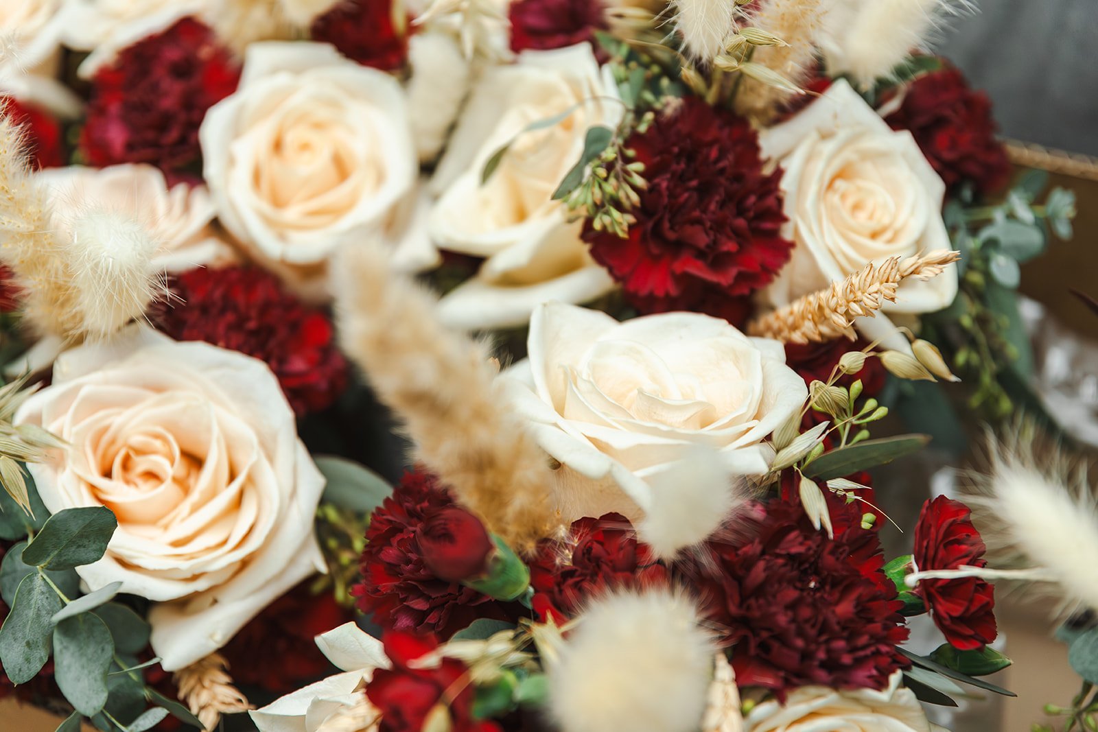 A close-up of a floral bouquet featuring white roses, red carnations, and other dried flowers and greenery.