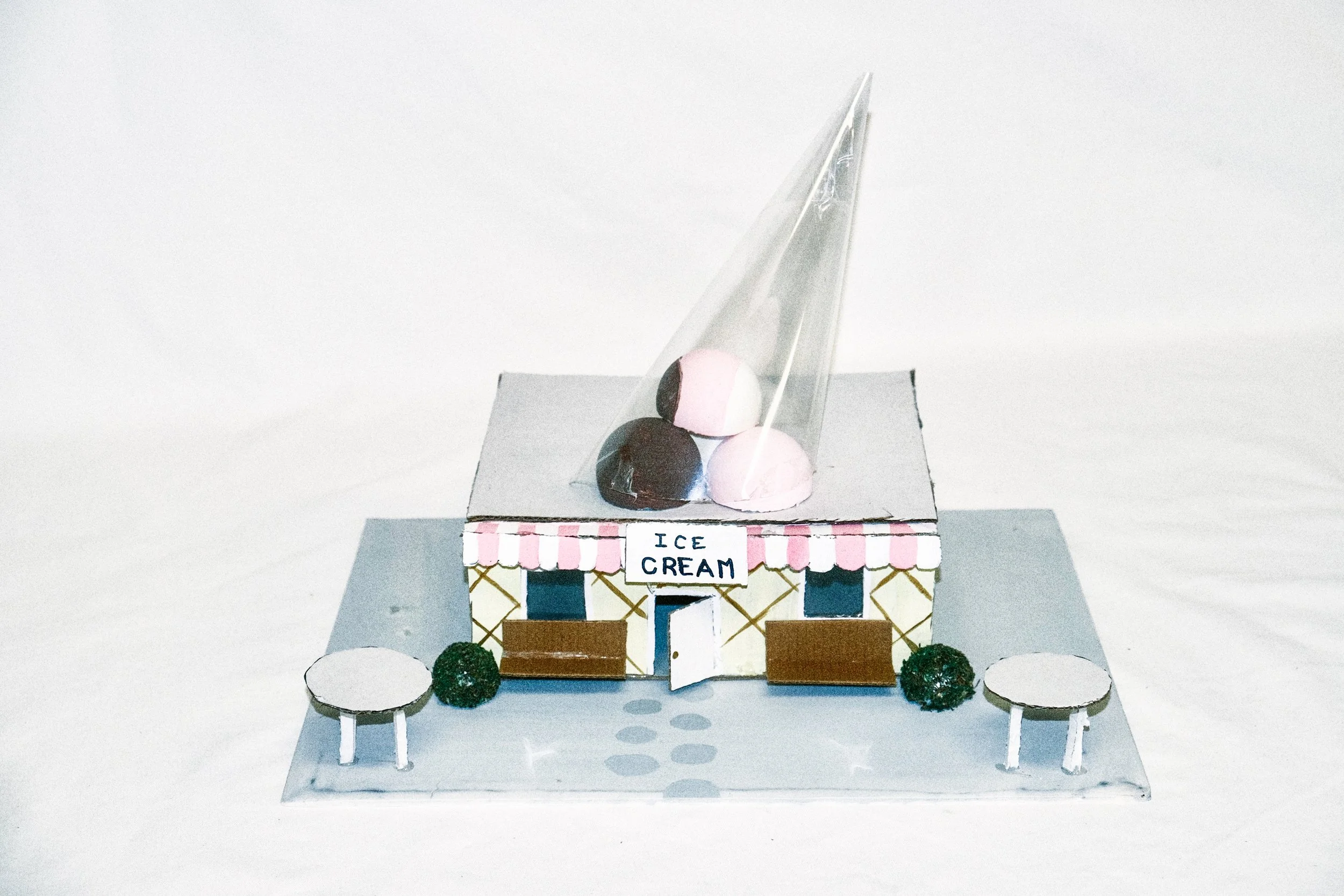 Miniature model of an ice cream shop with a sign that says open, two small ice cream cones on the roof, and outdoor seating