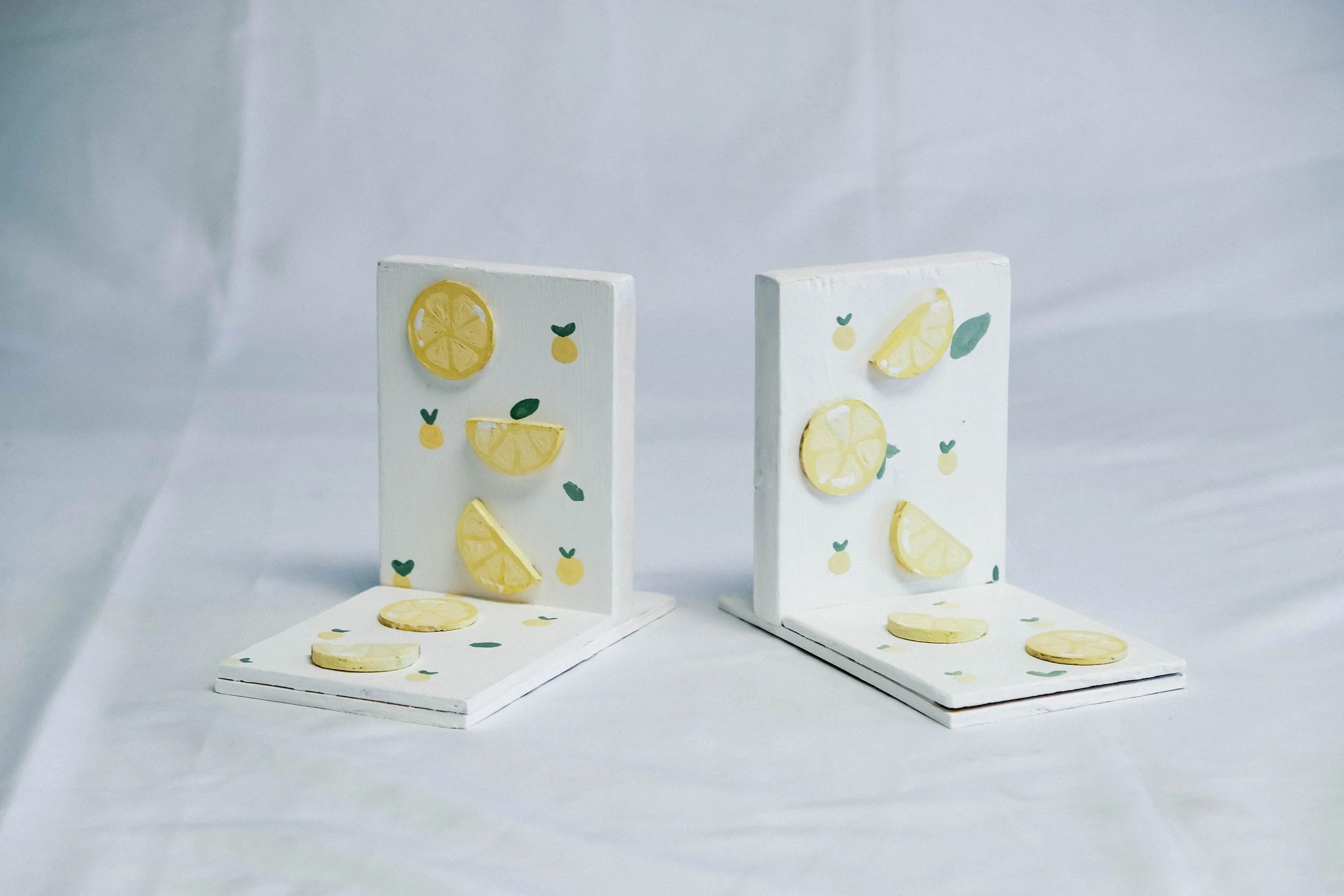 Decorative scene with miniature cardboard panels decorated with illustrations of lemon slices and lemon motifs, with some lemon slices placed on the panels and on the surface beneath.