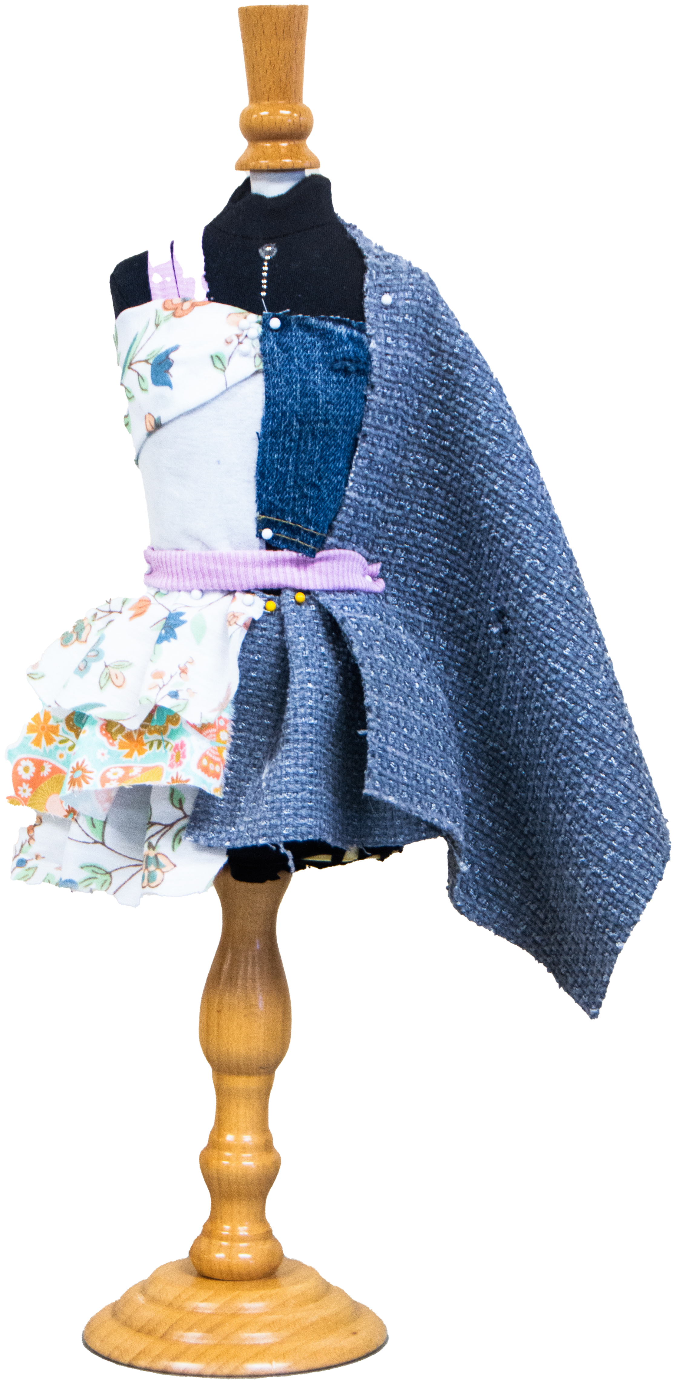 A mannequin dressed in a patchwork outfit consisting of fabrics in various patterns and textures, including floral, denim, knit, and tweed, styled with a black turtleneck top. The mannequin stands on a wooden base and has a beige background.