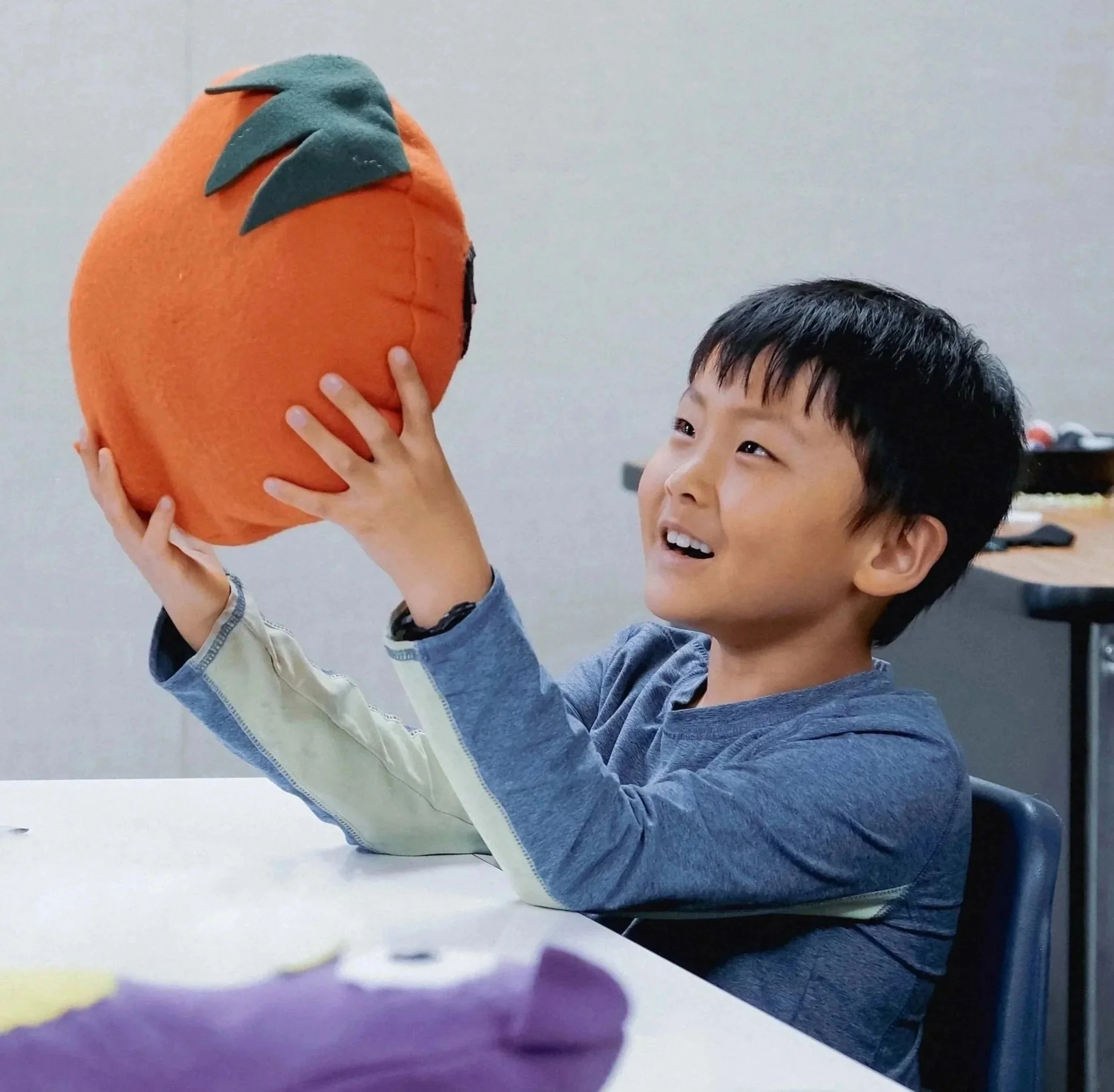 A young boy holding a plush pumpkin with a smile.