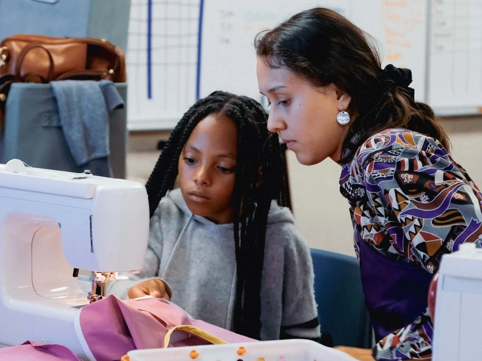 A woman and a girl sewing together, with the woman guiding the girl on a sewing machine.