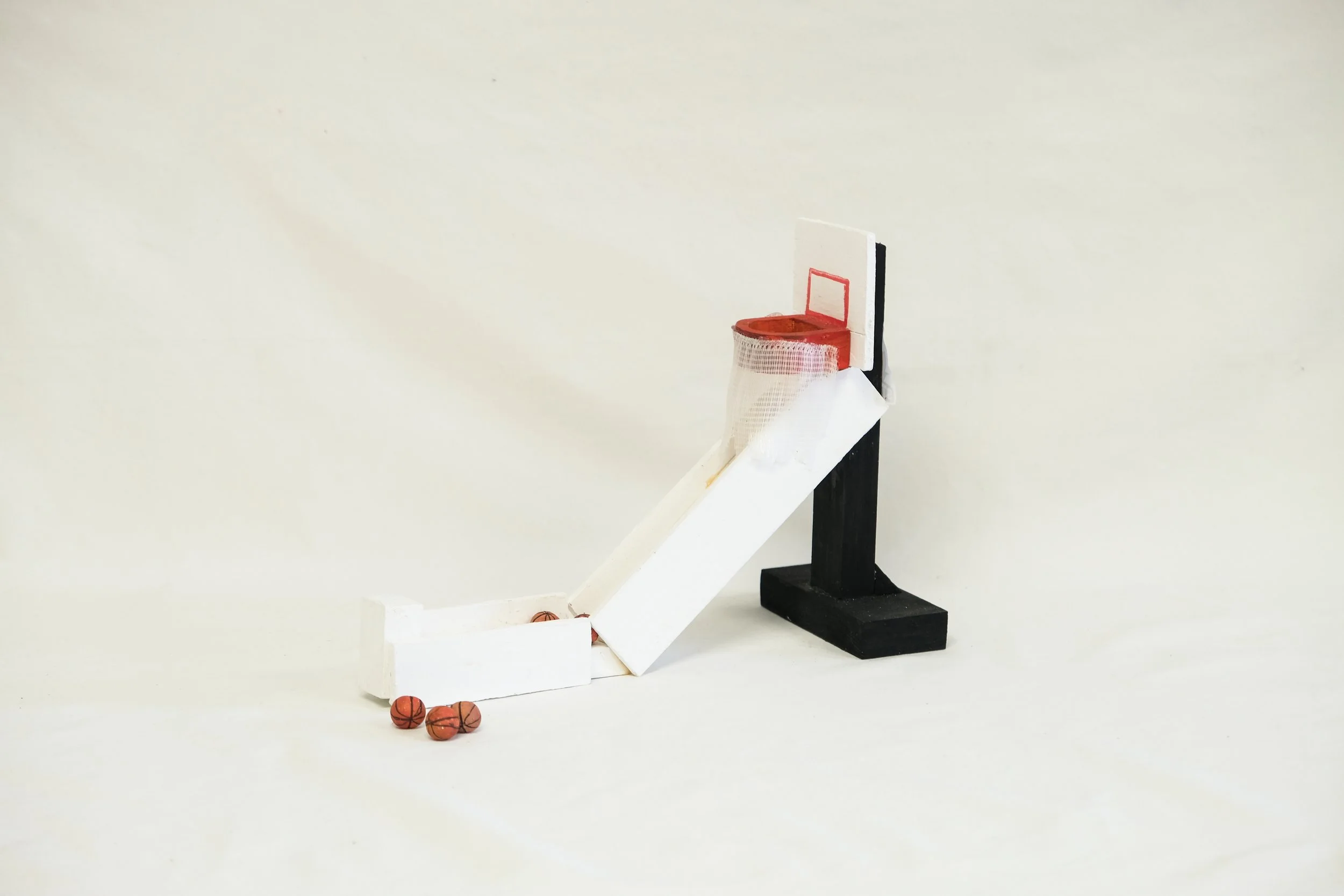Miniature basketball arcade toy with a white ramp, red hoop, and a black stand, with miniature basketballs