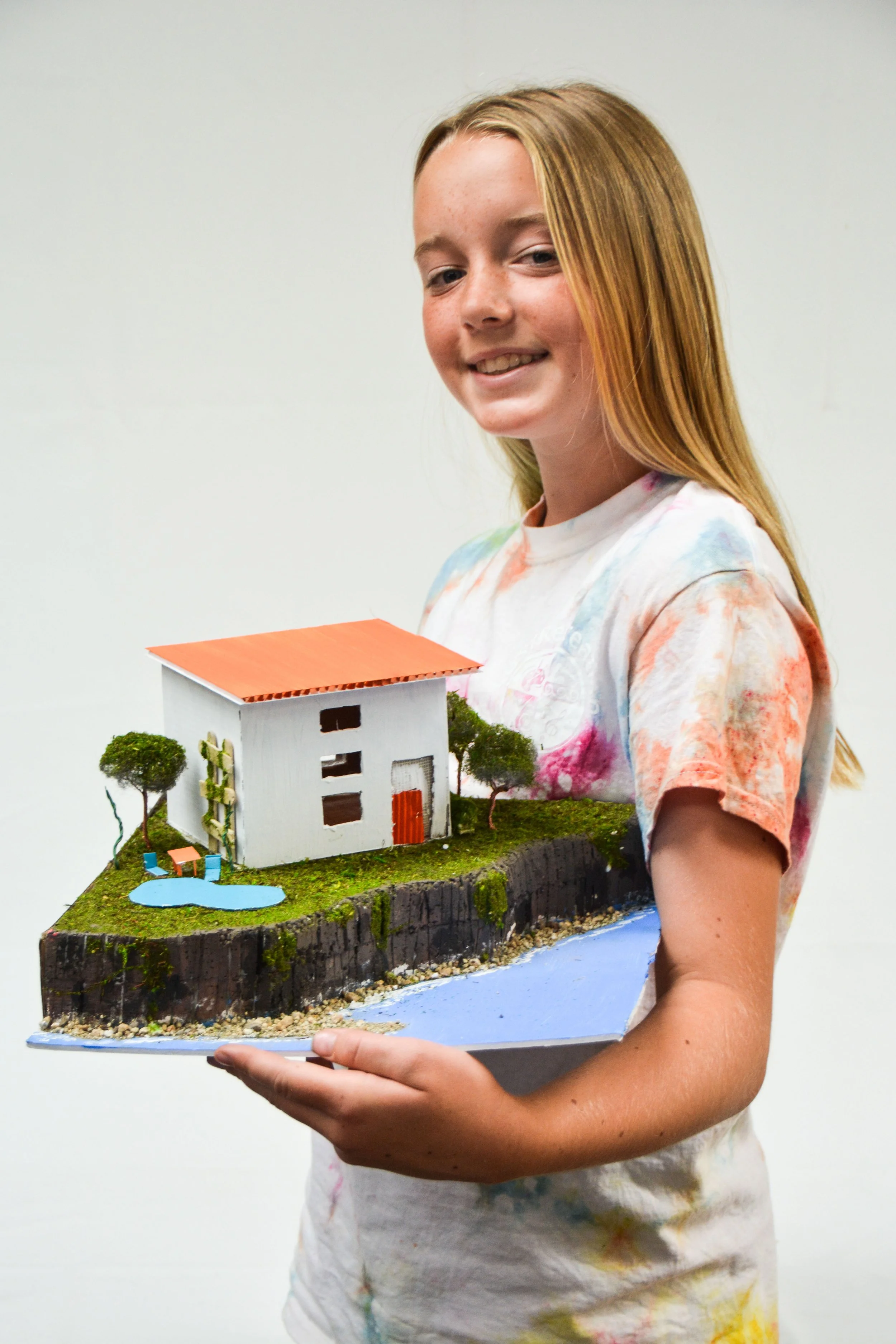 A young girl holding a detailed miniature model of a house with a pond and trees.