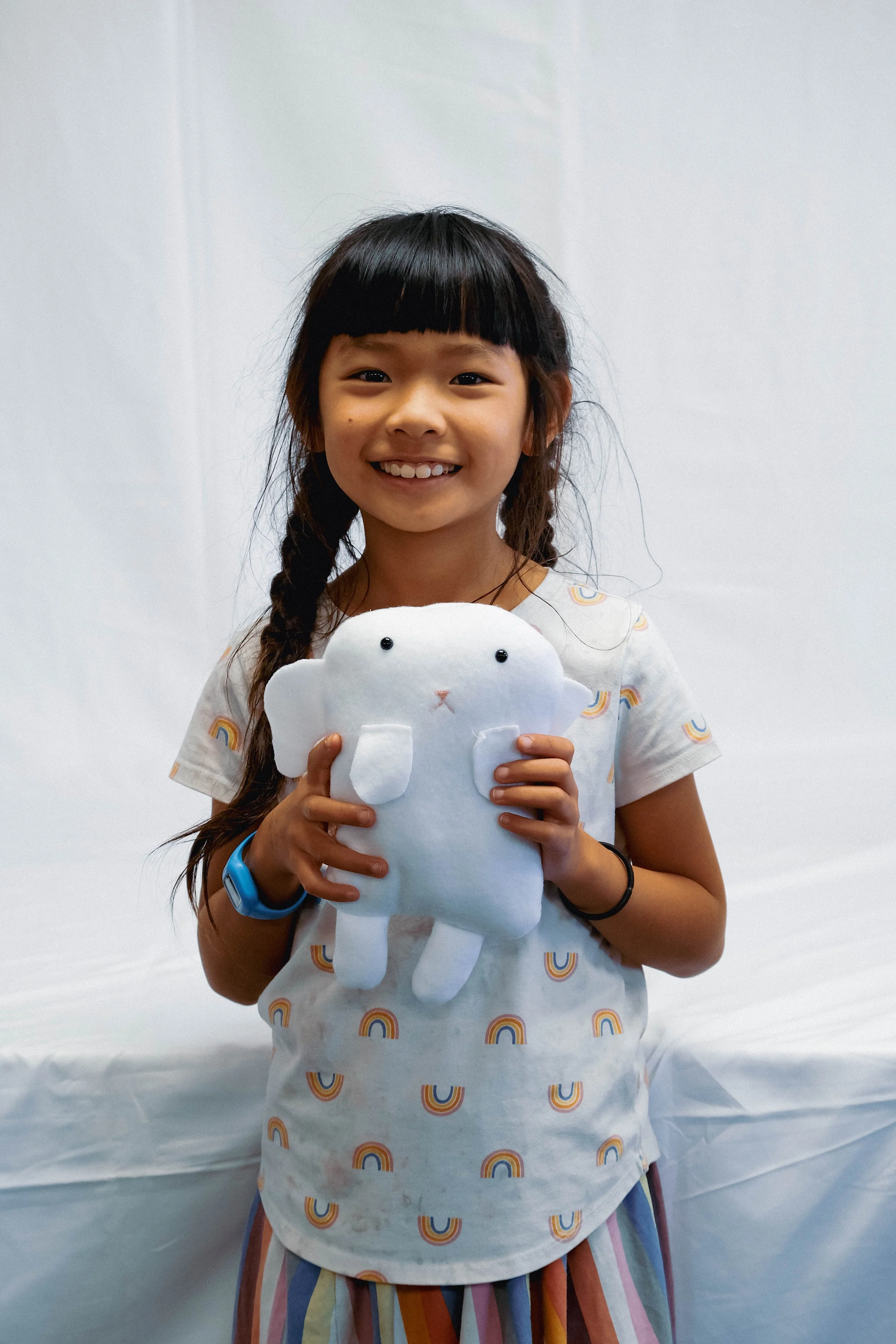 A young girl smiling and holding a white plush toy that resembles a cat.