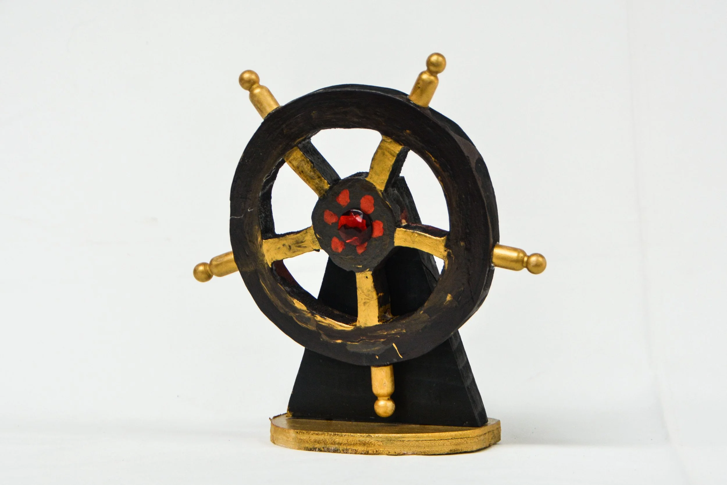 Decorative ship's helm with black and gold colors on a black stand against a white background.