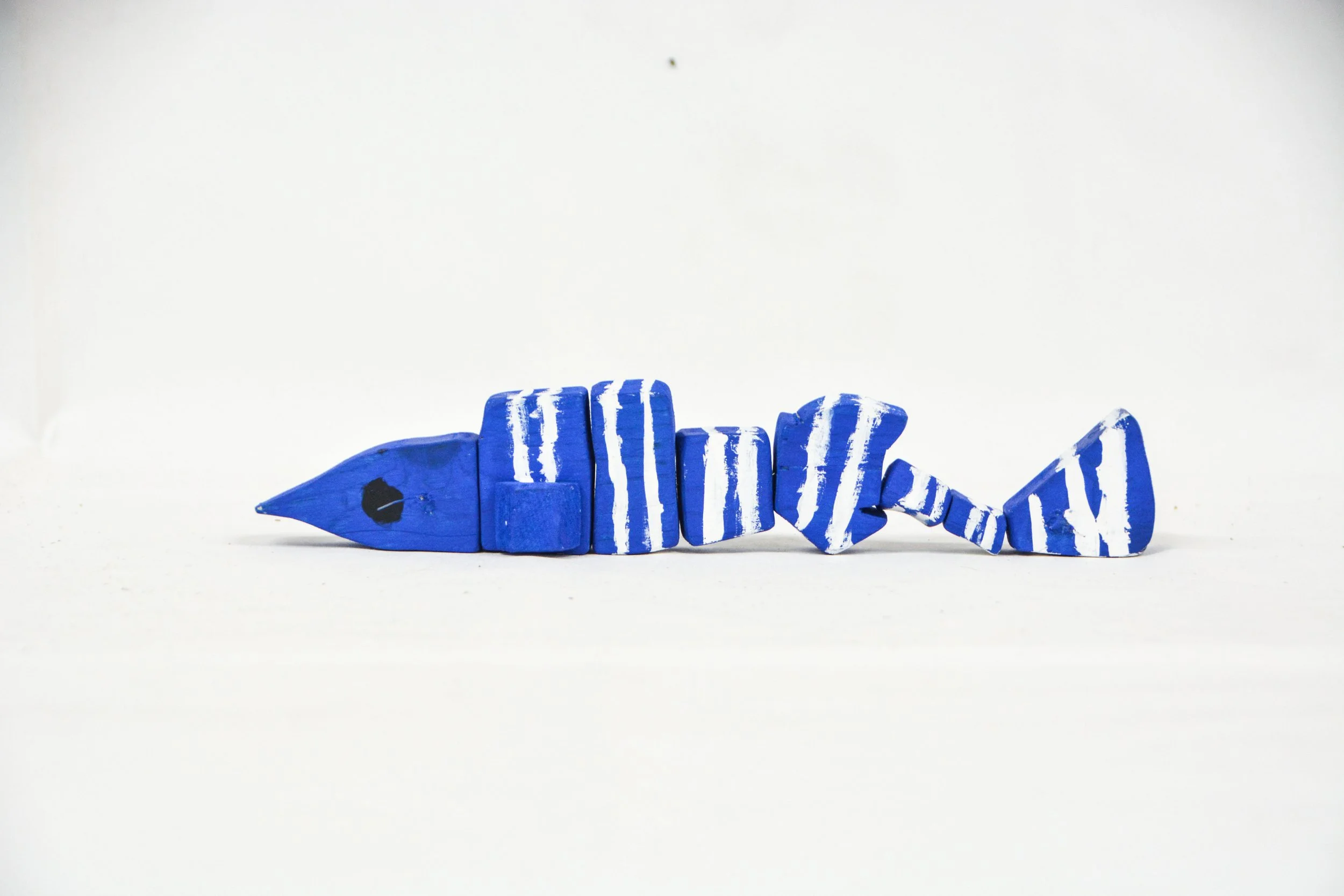 Blue spiral-shaped wooden fish carved with white stripes and a black eye, lying on a white surface, made by designx student on the wood toy design program