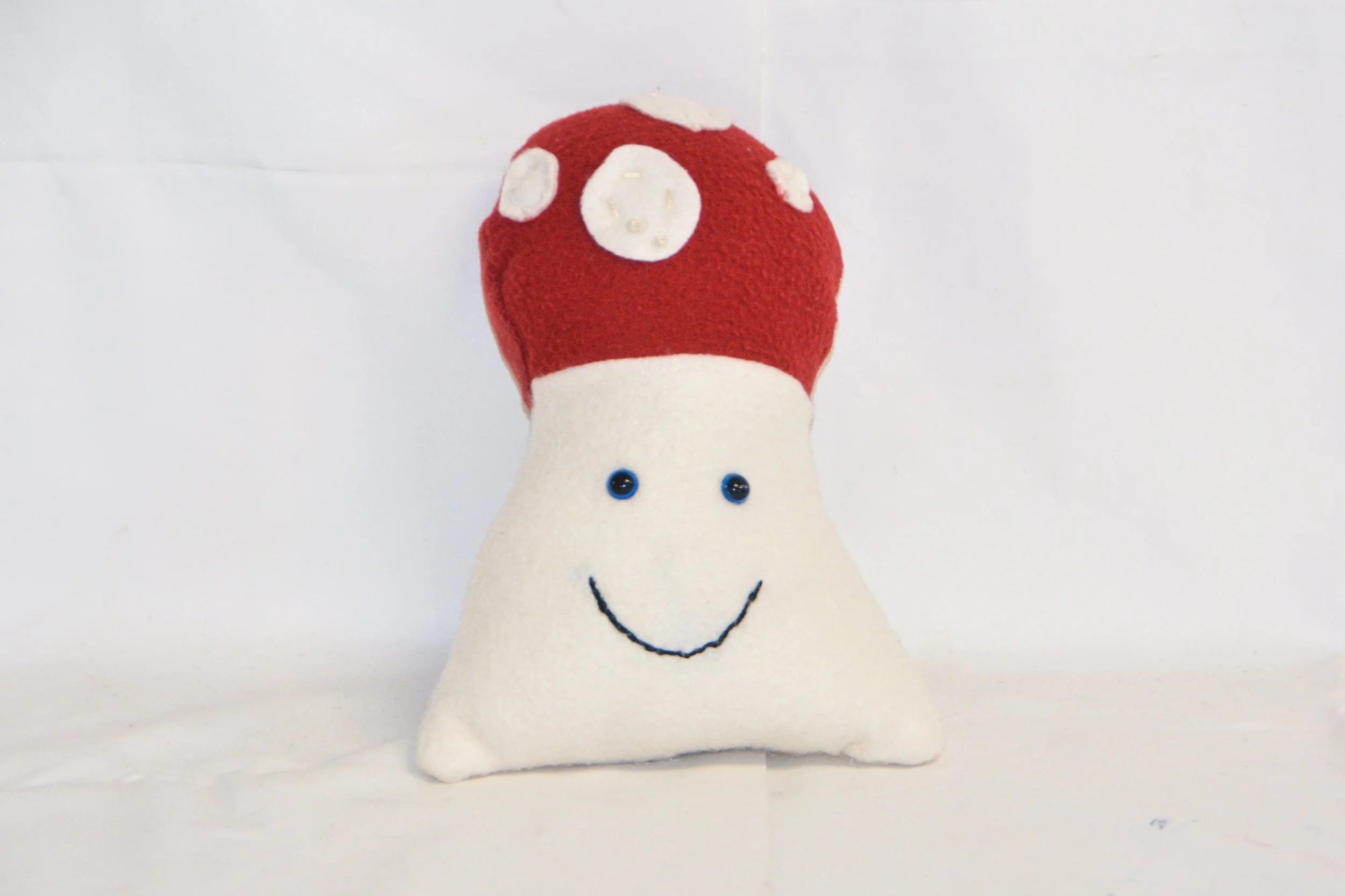 Cute plush toy resembling a smiling mushroom with a red and white cap and a white stem, set against a plain white background.