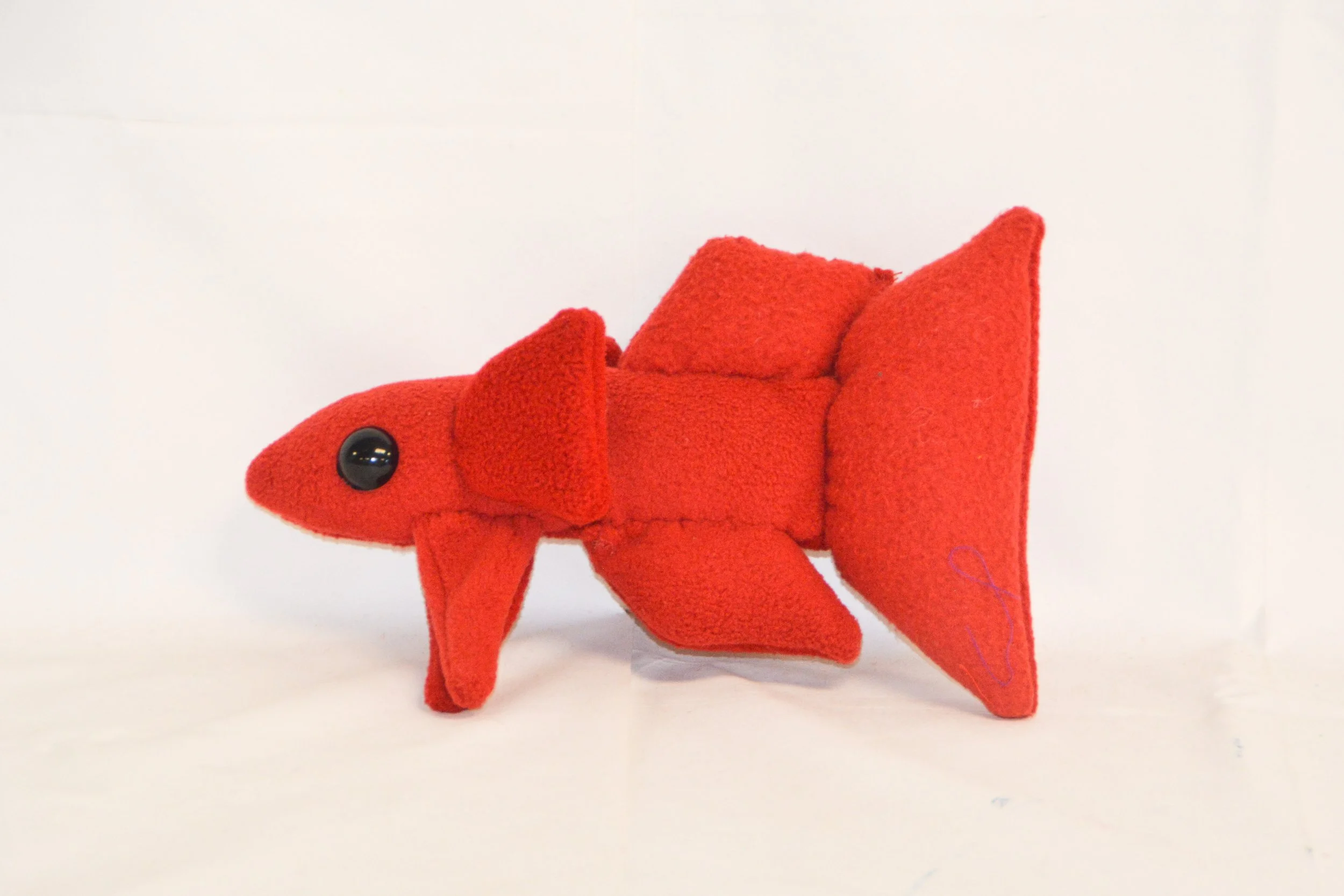 Red plush fish toy with black eyes, set against a plain white background.