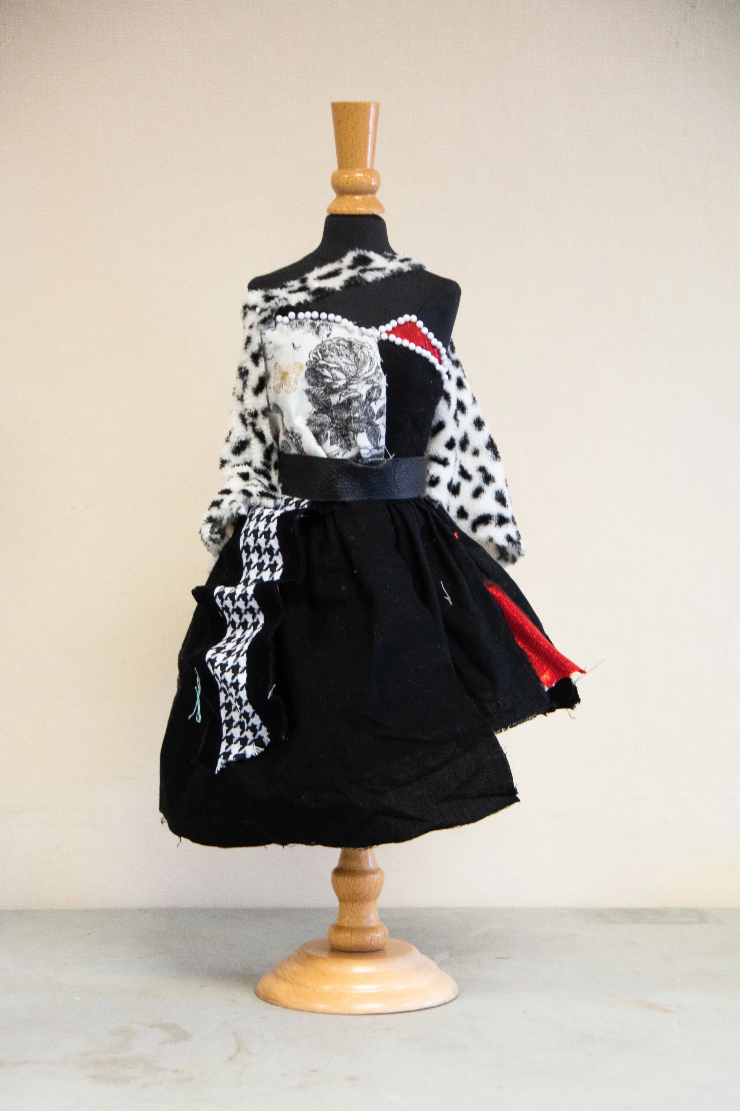 A dress form displaying a black, white, and red dress with various fabric patterns and embellishments, including leopard print, houndstooth, and graphic prints.