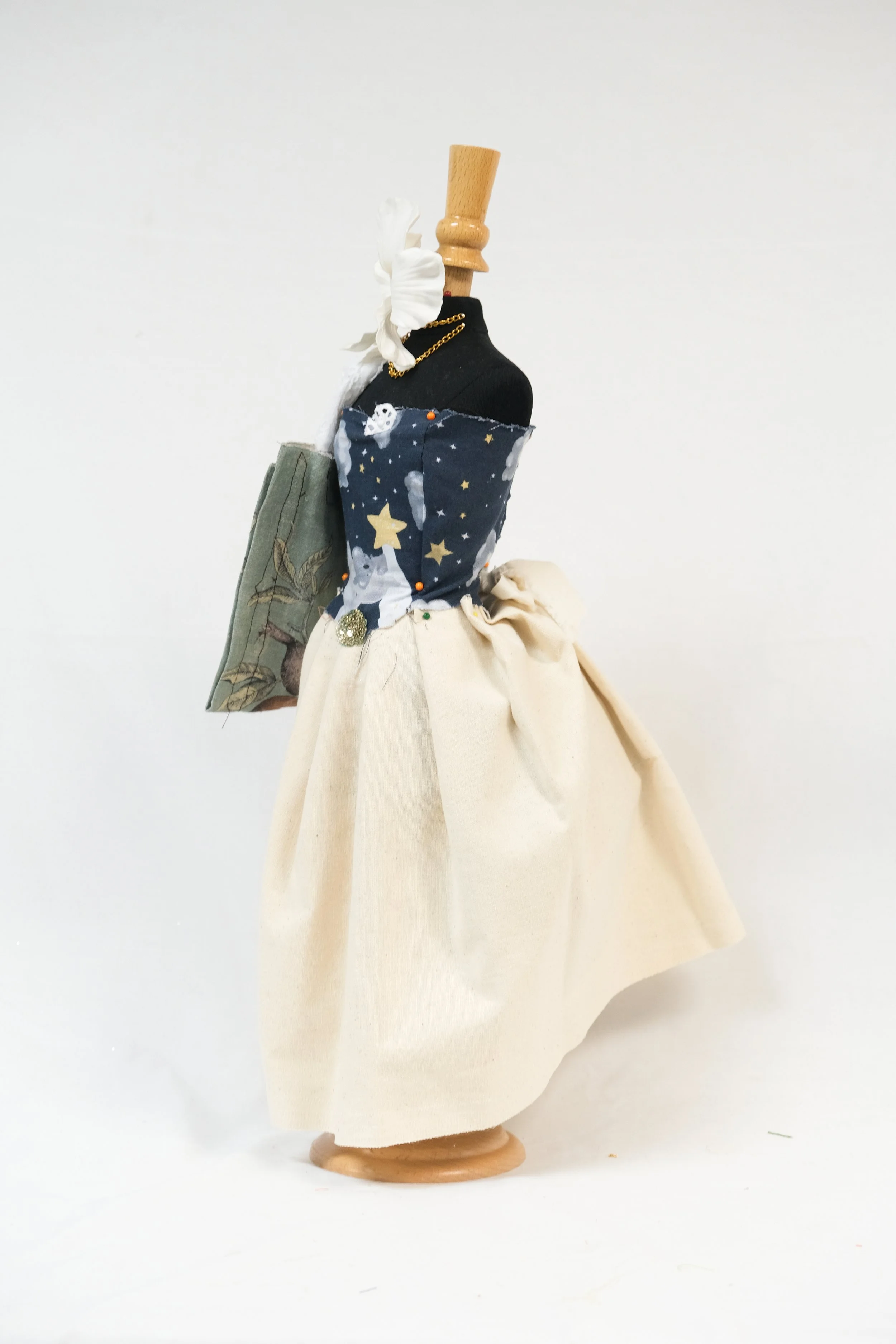 A mannequin dressed in a handmade fantasy-inspired outfit with a black torso, a starry night sky patterned top, cream-colored full skirt, and various fabric accessories.